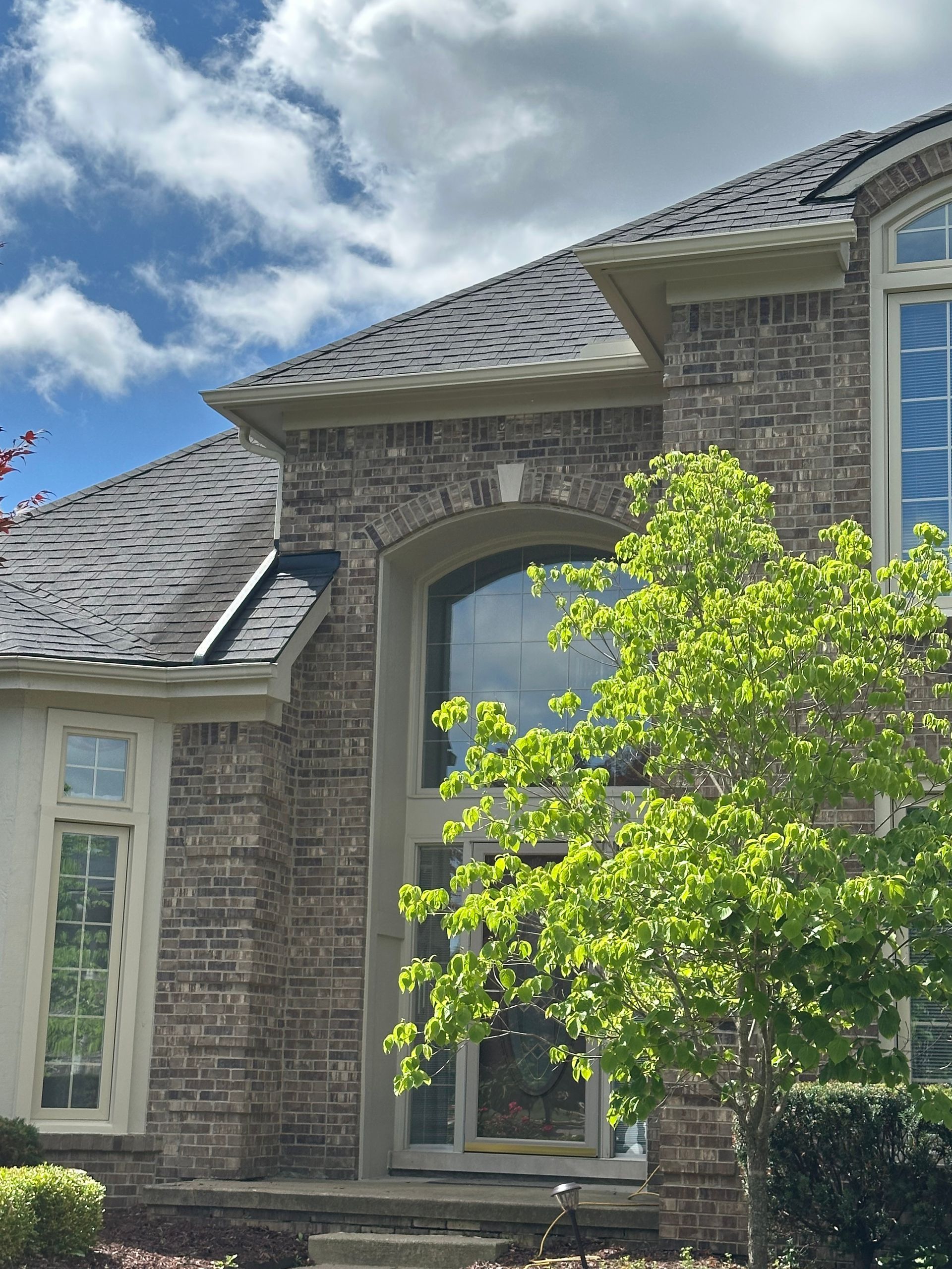 Brick house with dark roof and large arched window. Green tree in the foreground.