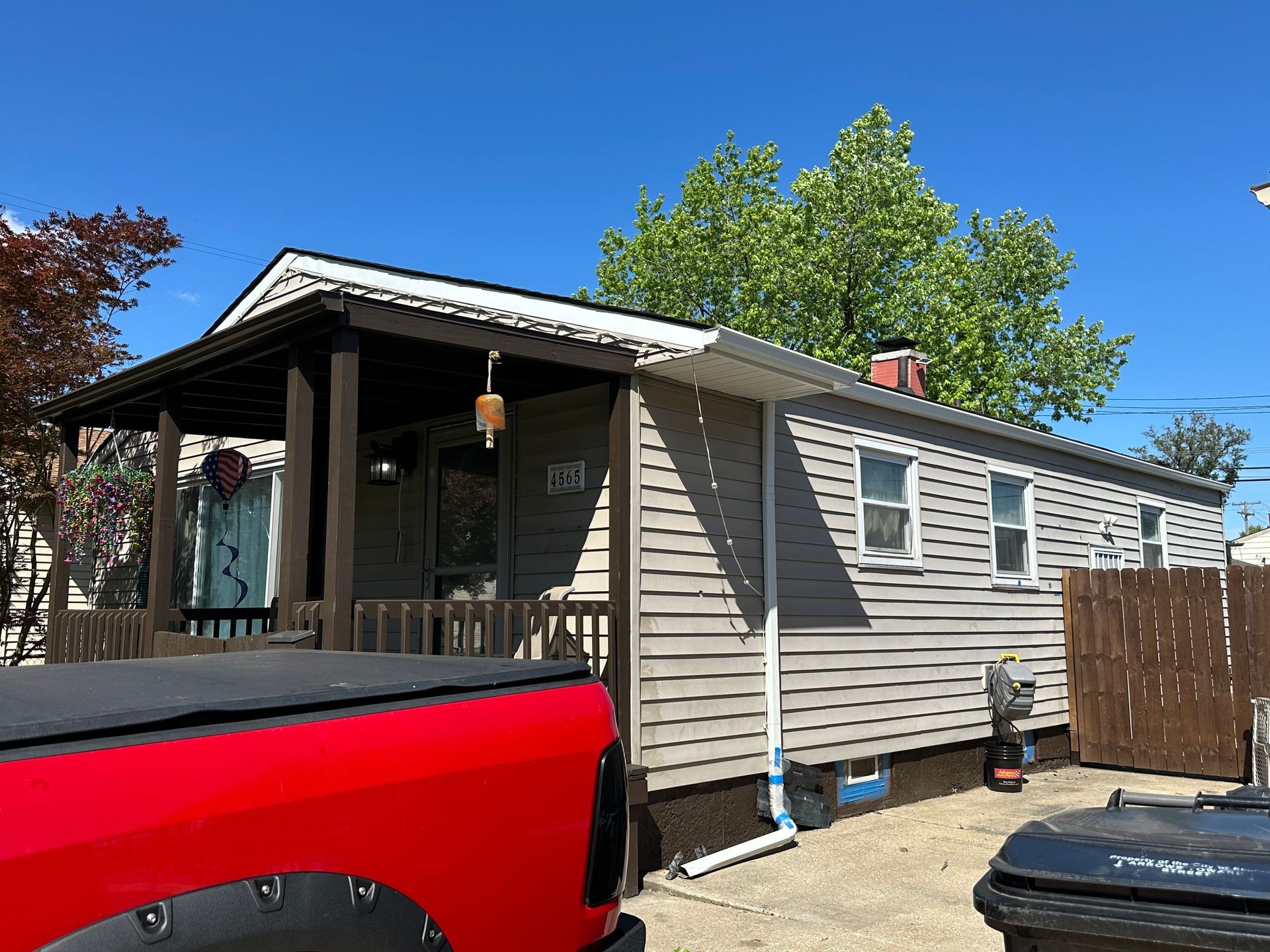 A gray house with a porch, red truck parked in front, and blue sky.