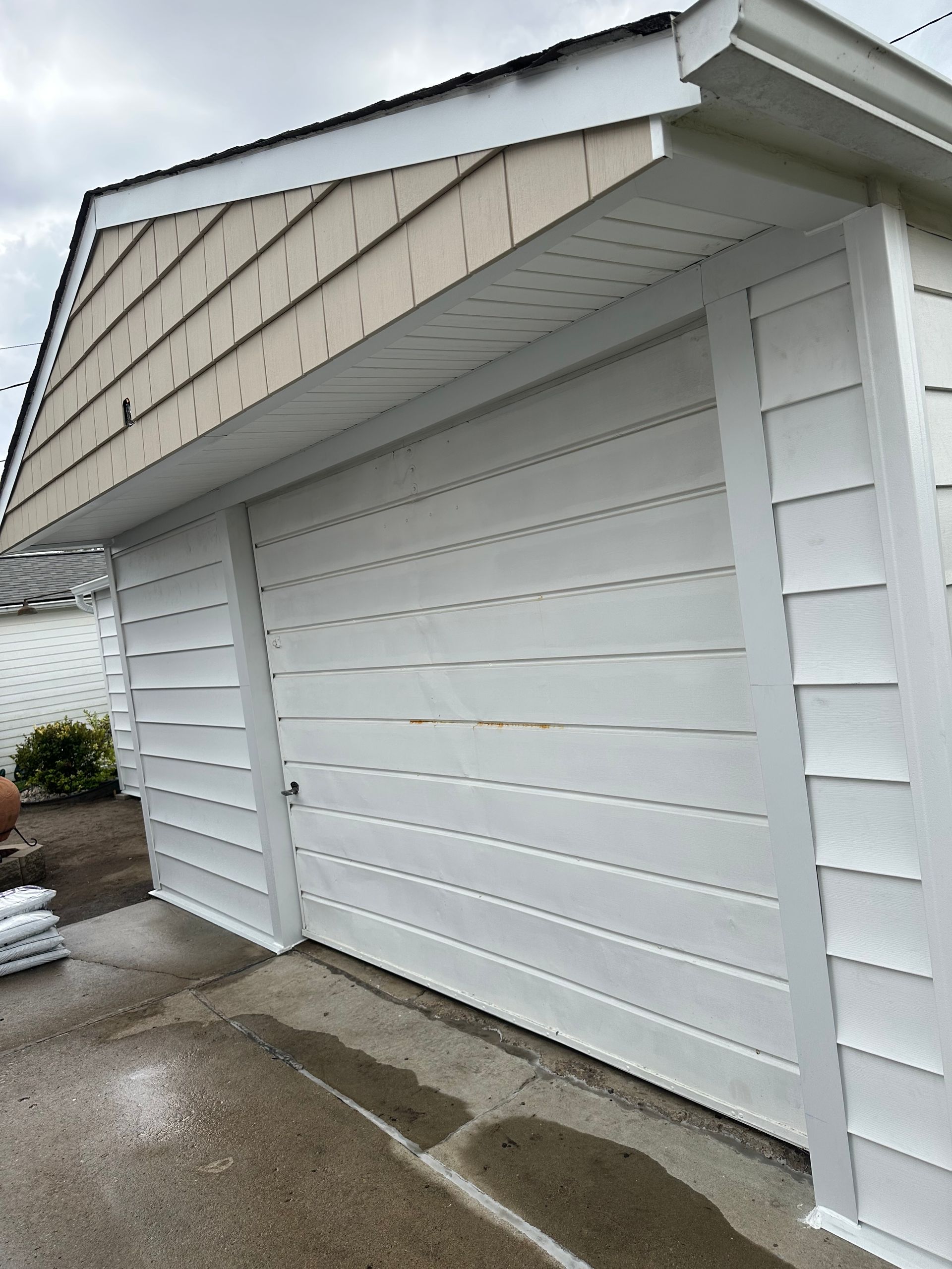 White-sided garage with closed door; tan siding above the white. Concrete driveway in front.