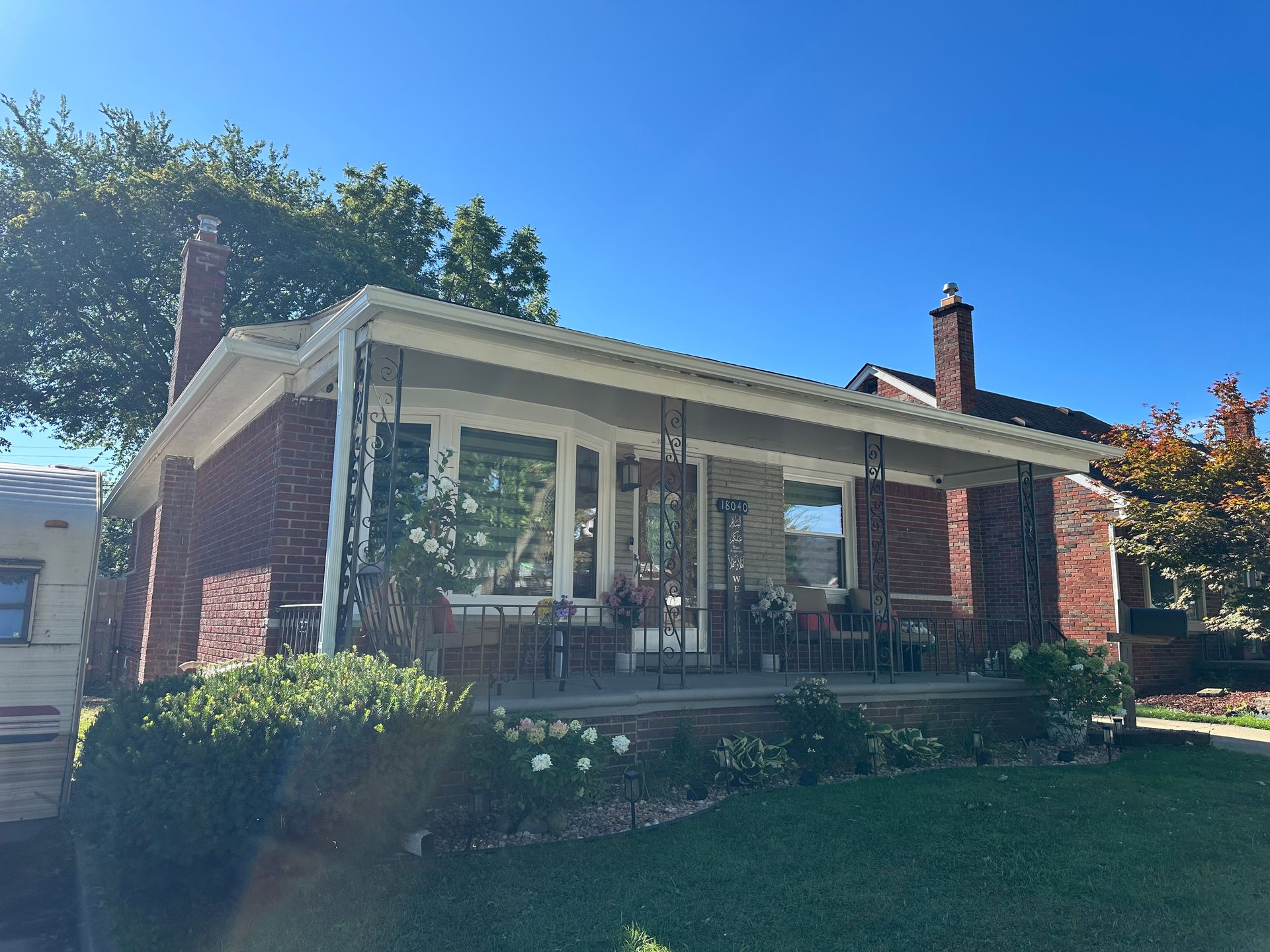 Brick house with a front porch, green lawn, and blue sky.