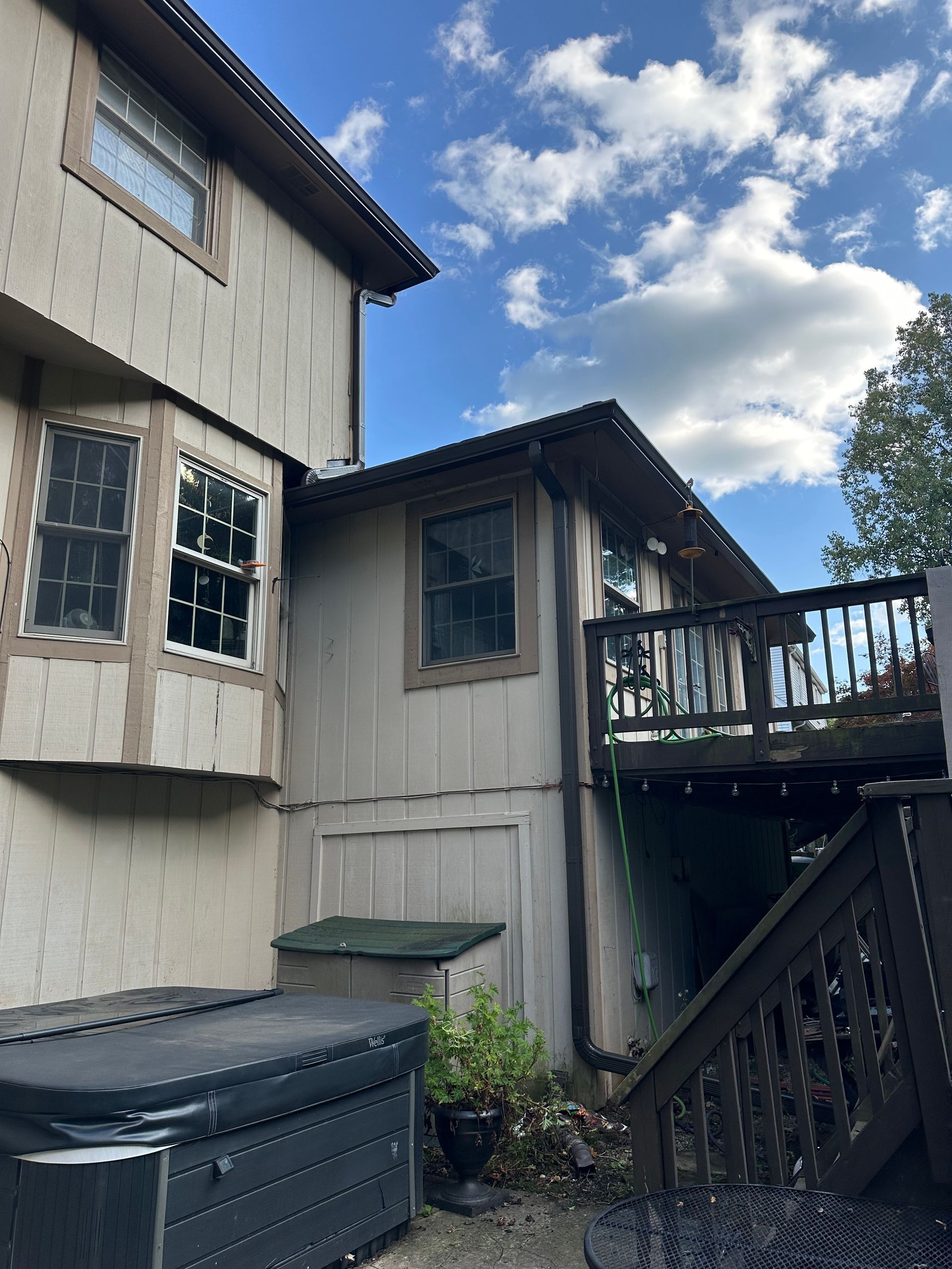 Exterior view of a house with a deck. Beige siding, brown trim, and a blue sky with clouds are visible.