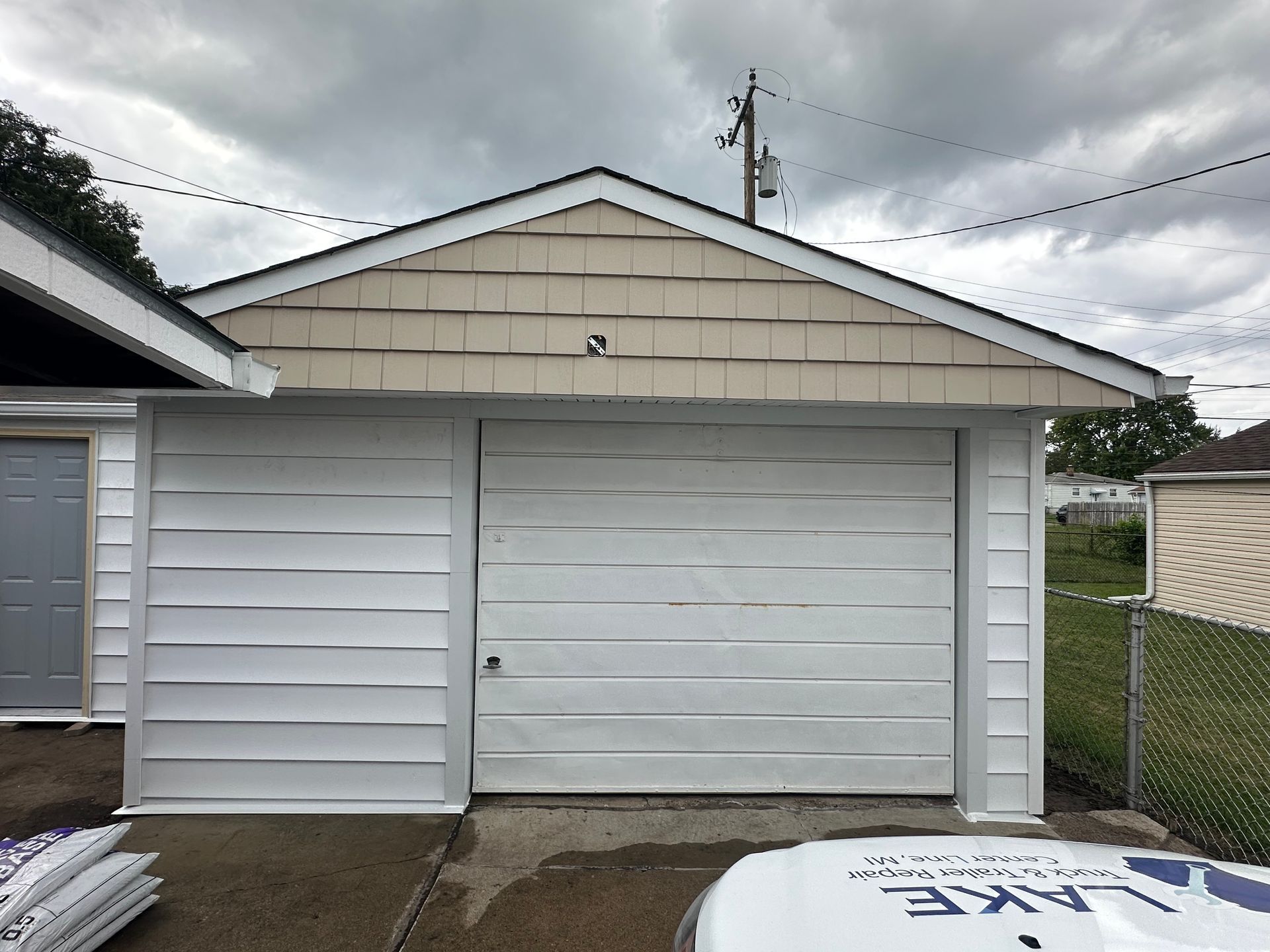 White garage with a light tan shingled gable under a cloudy sky.