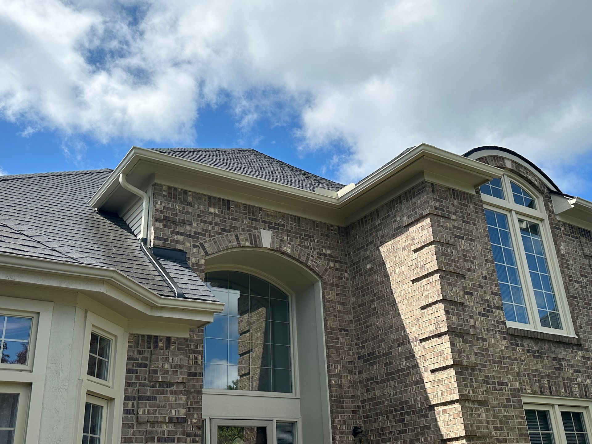 Brick house exterior with dark roof and blue sky.