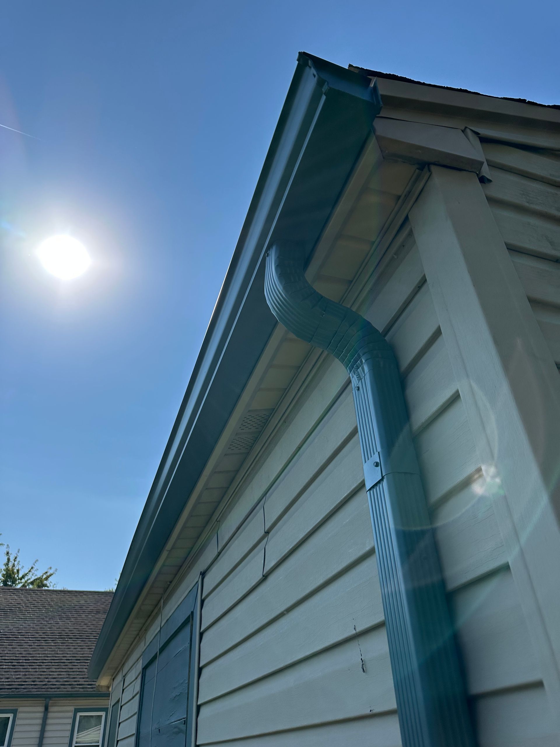 Blue gutters and downspout on a light-colored building under a bright, sunny sky.