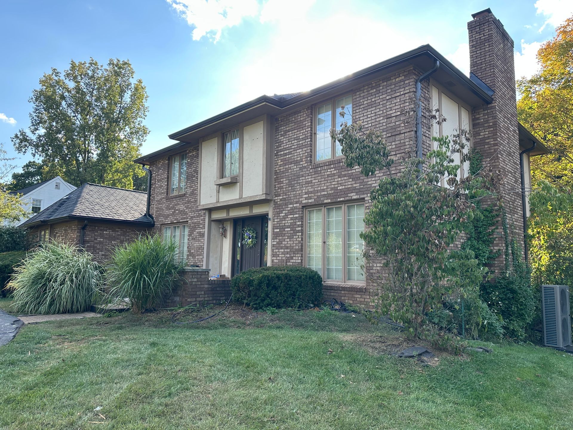 Two-story brick house with beige trim, a chimney, and a small yard.