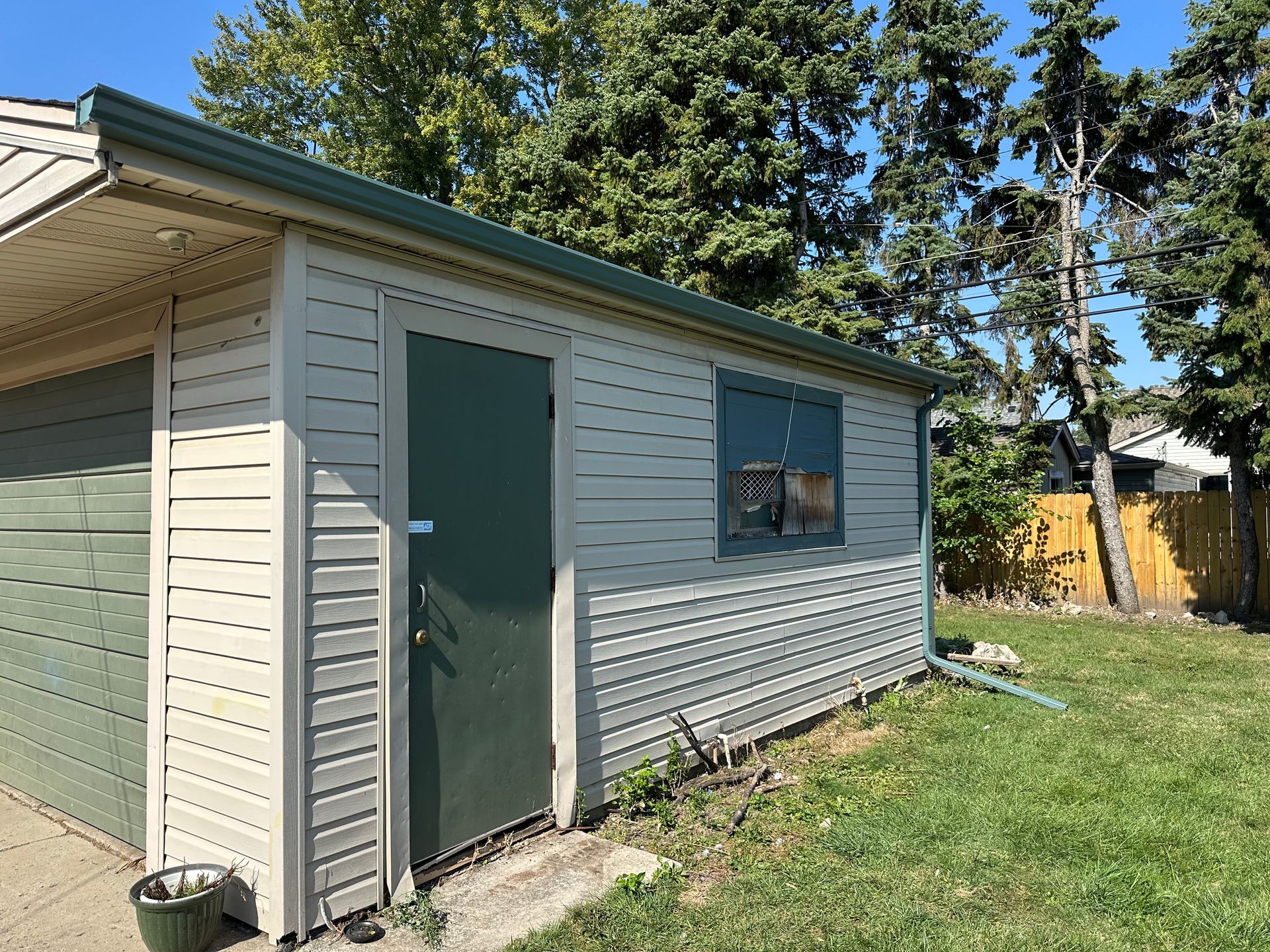 Storage shed with green door and window; beige siding, green trim, and grass.
