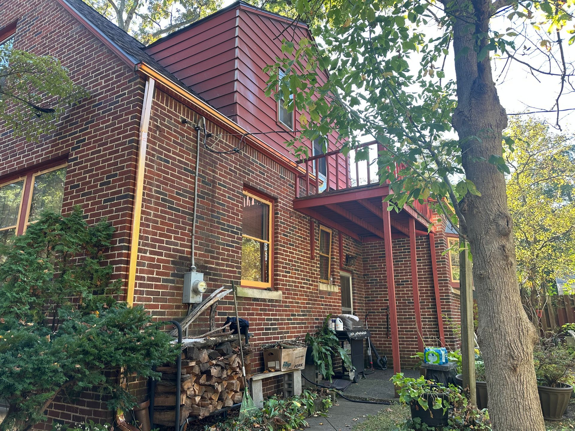 Brick house with a red-painted side entrance and small balcony; firewood and grill are visible.