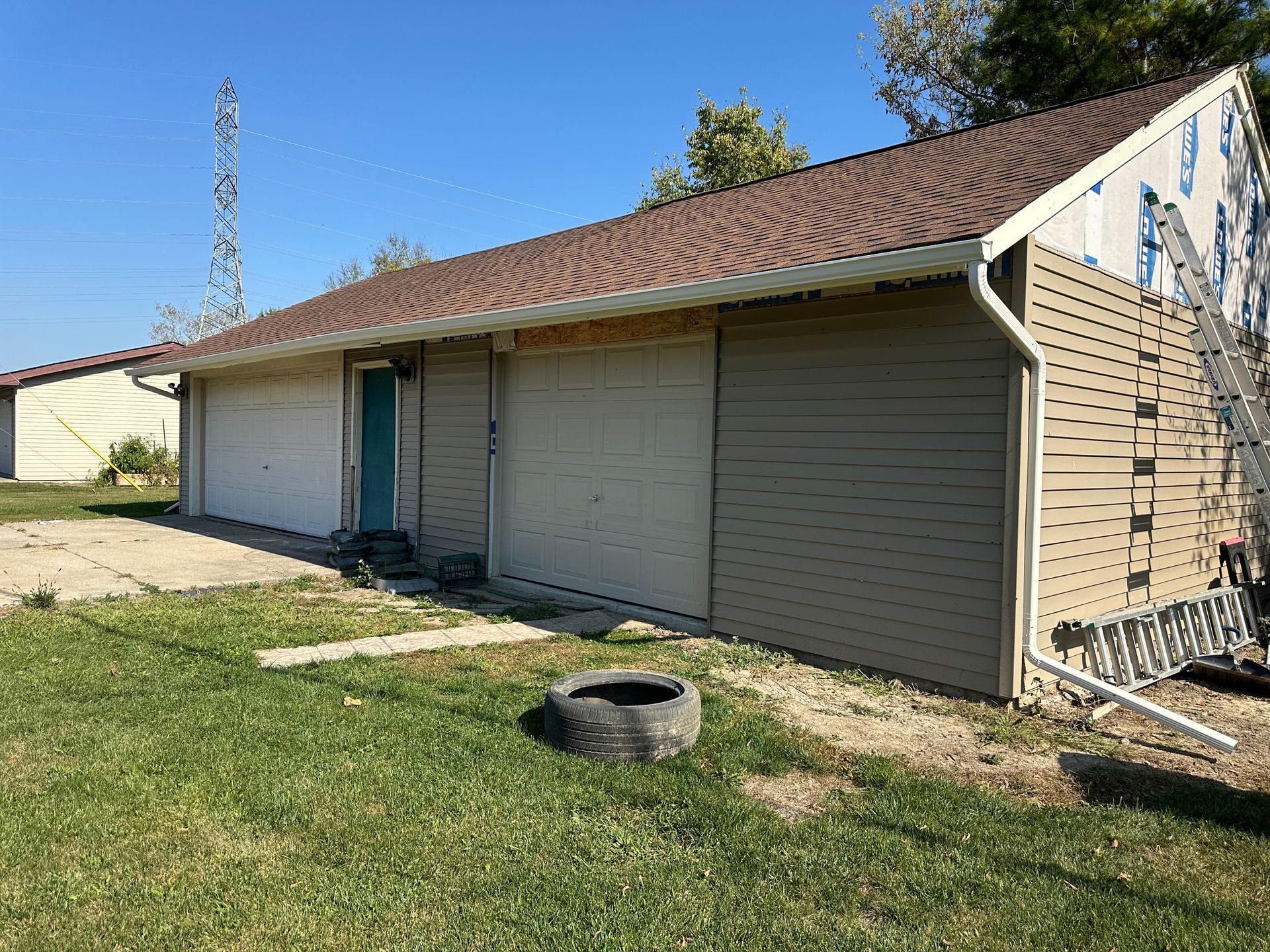Garage with two doors, new siding, brown roof, and tire in the yard.