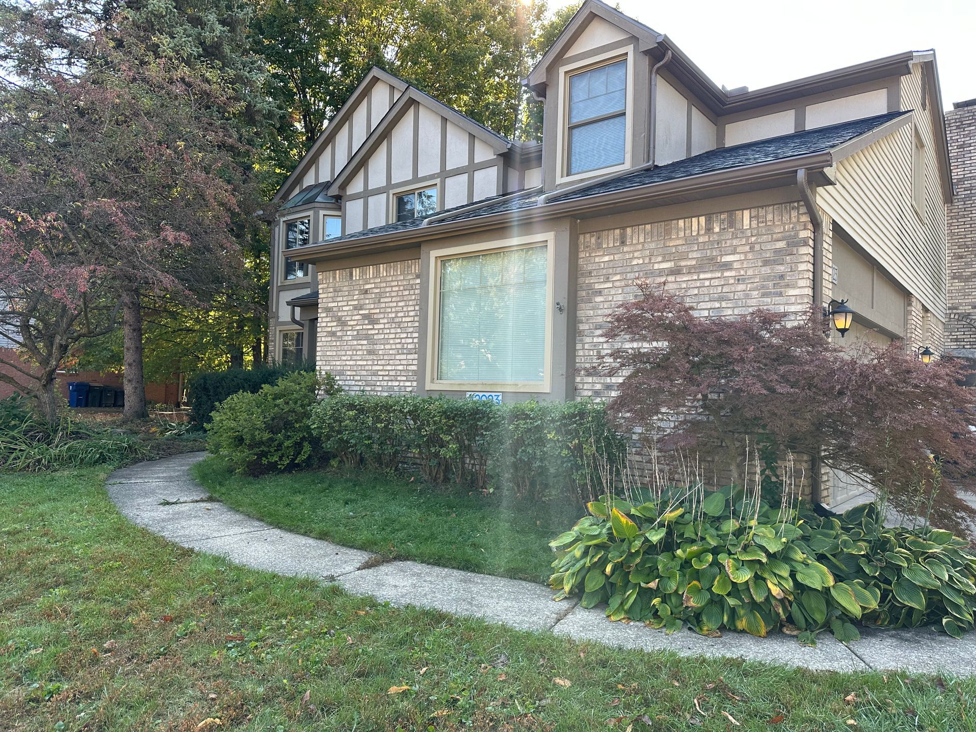 Tudor-style house with brick and siding, a pathway, and landscaping on a grassy lawn.
