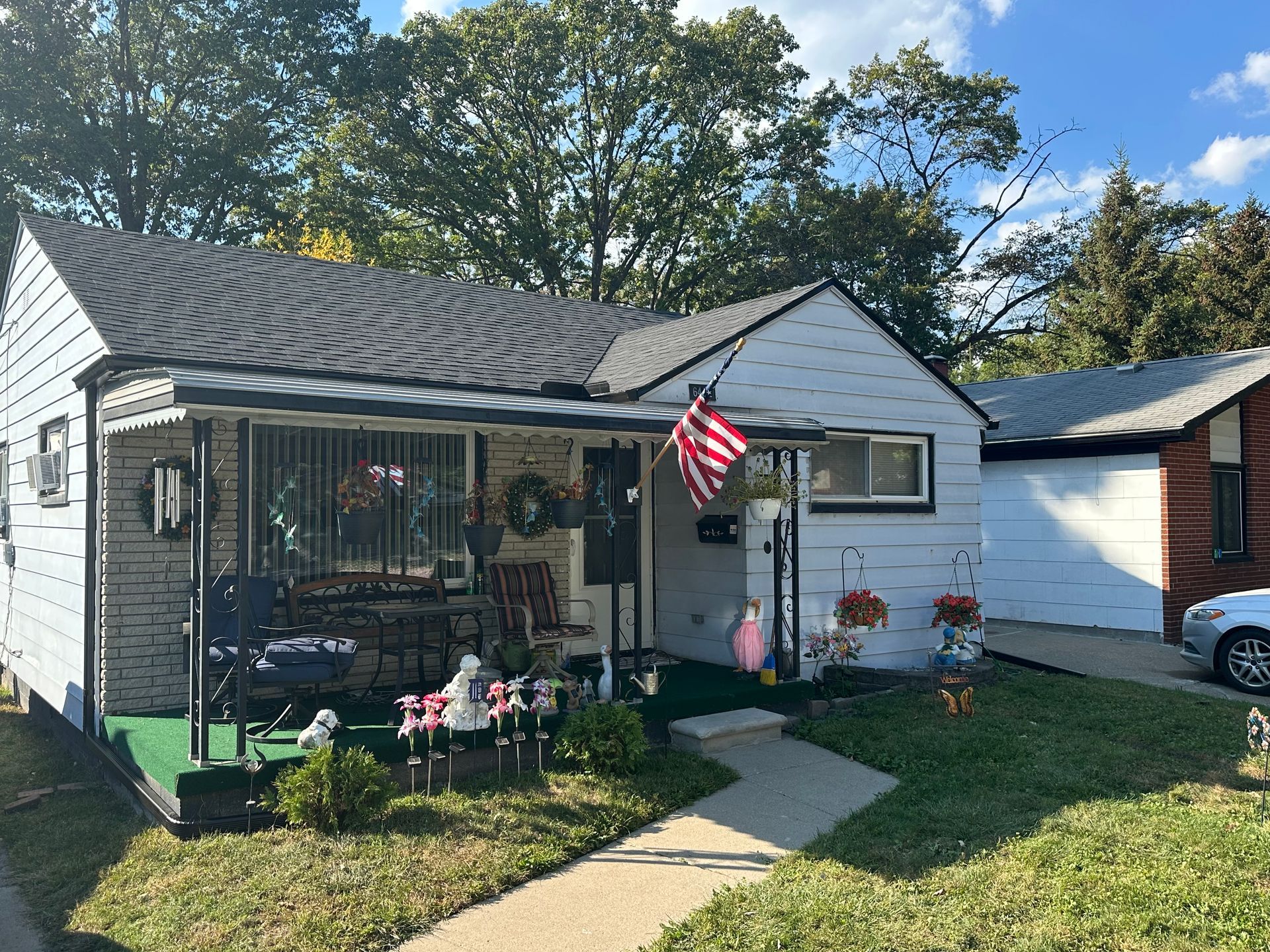 White house with black trim, porch, American flag, lawn, and garage on a sunny day.