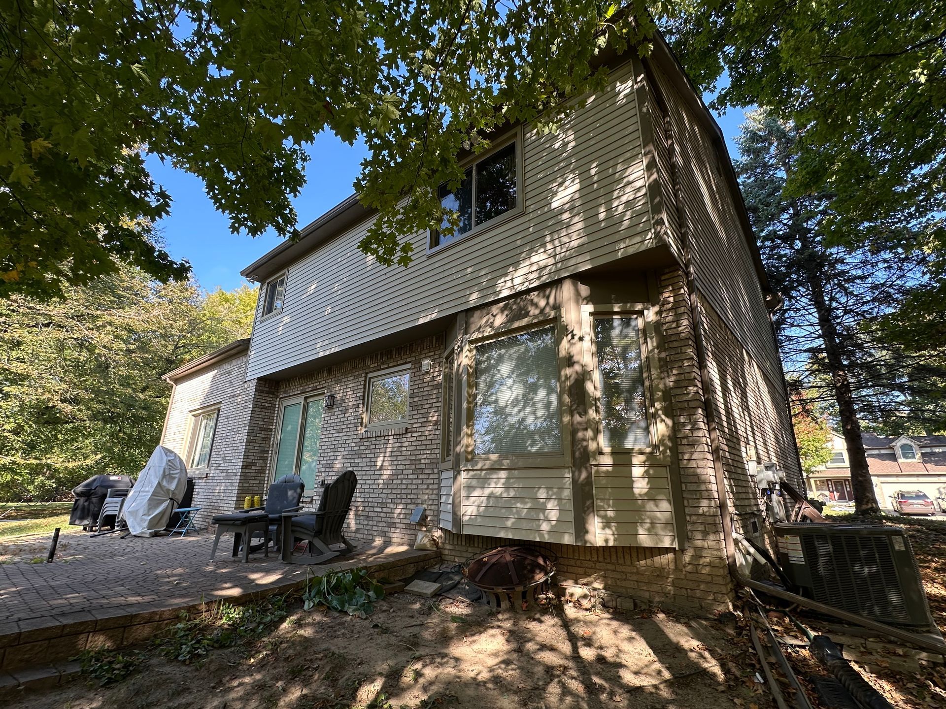 House exterior with stone and siding, surrounded by trees and a patio.