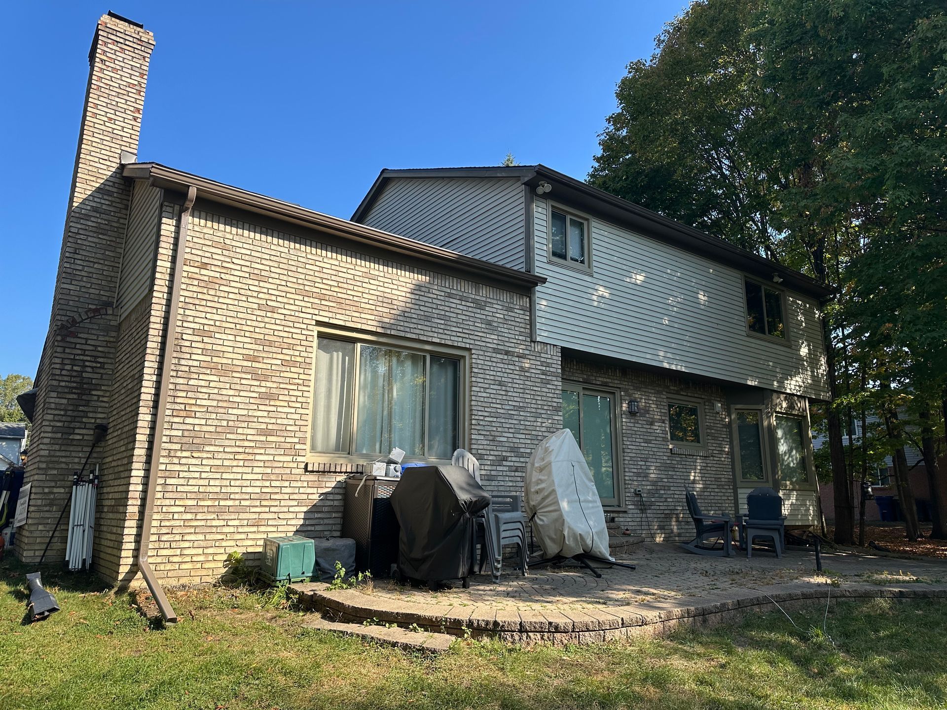 Two-story house exterior with brick chimney and siding, small patio, and backyard.