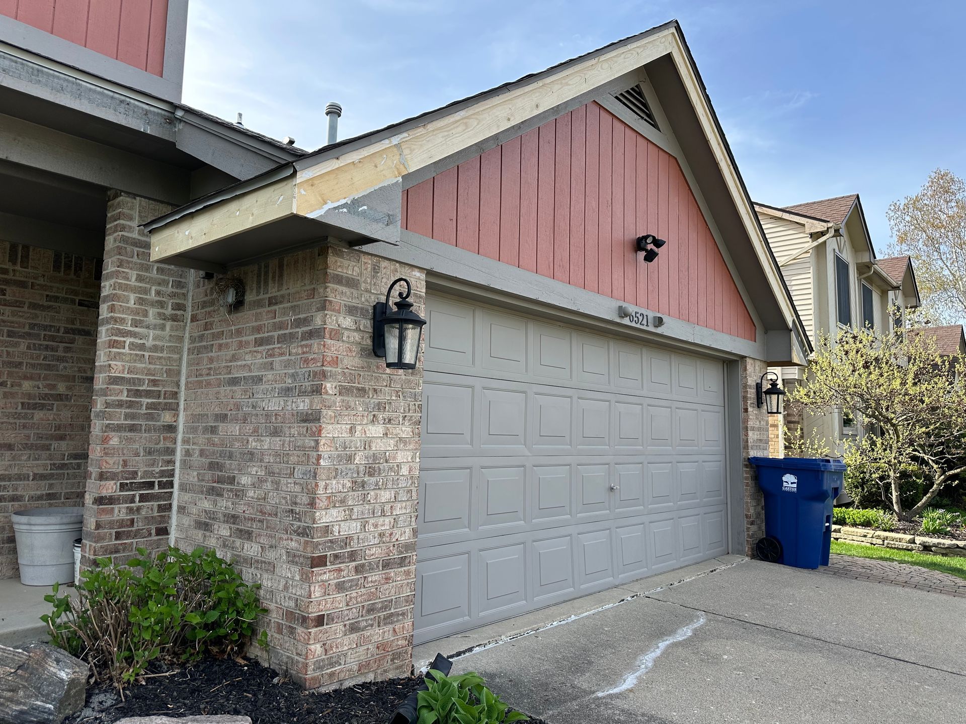Garage with gray door, brick exterior, and reddish-brown gable siding. Two black sconces flank the door.