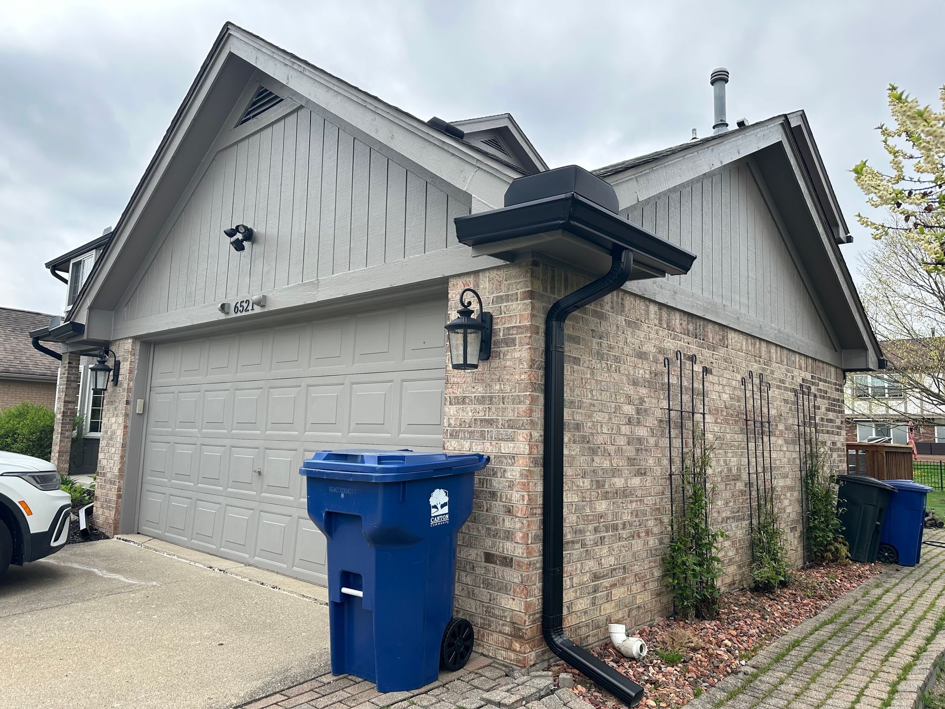 Garage with grey door, brick walls, and black gutters. A blue trash bin is in front.