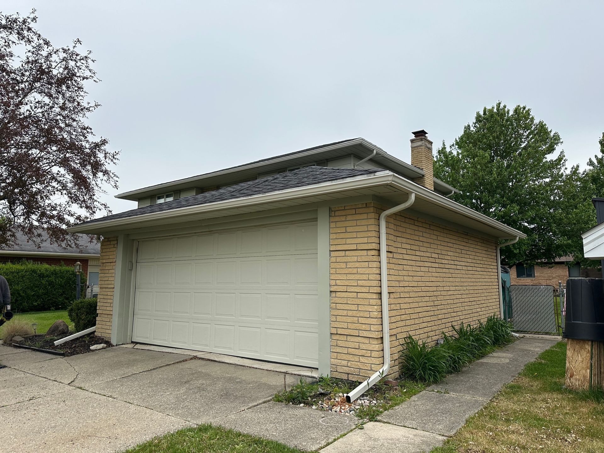 Brick garage with a gray roof and a closed white garage door; overcast day.