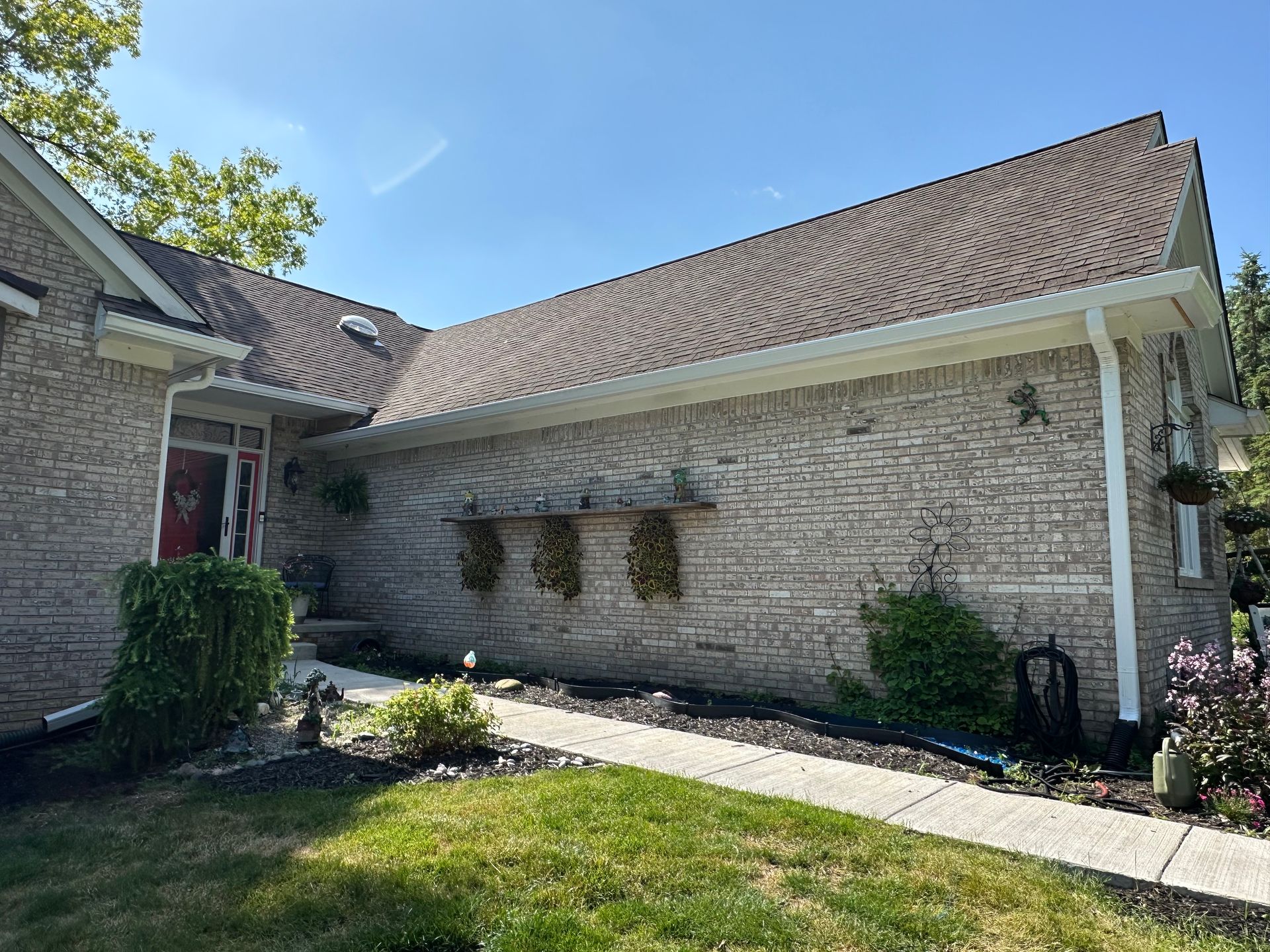 Brick house exterior with brown roof and white trim under a blue sky.