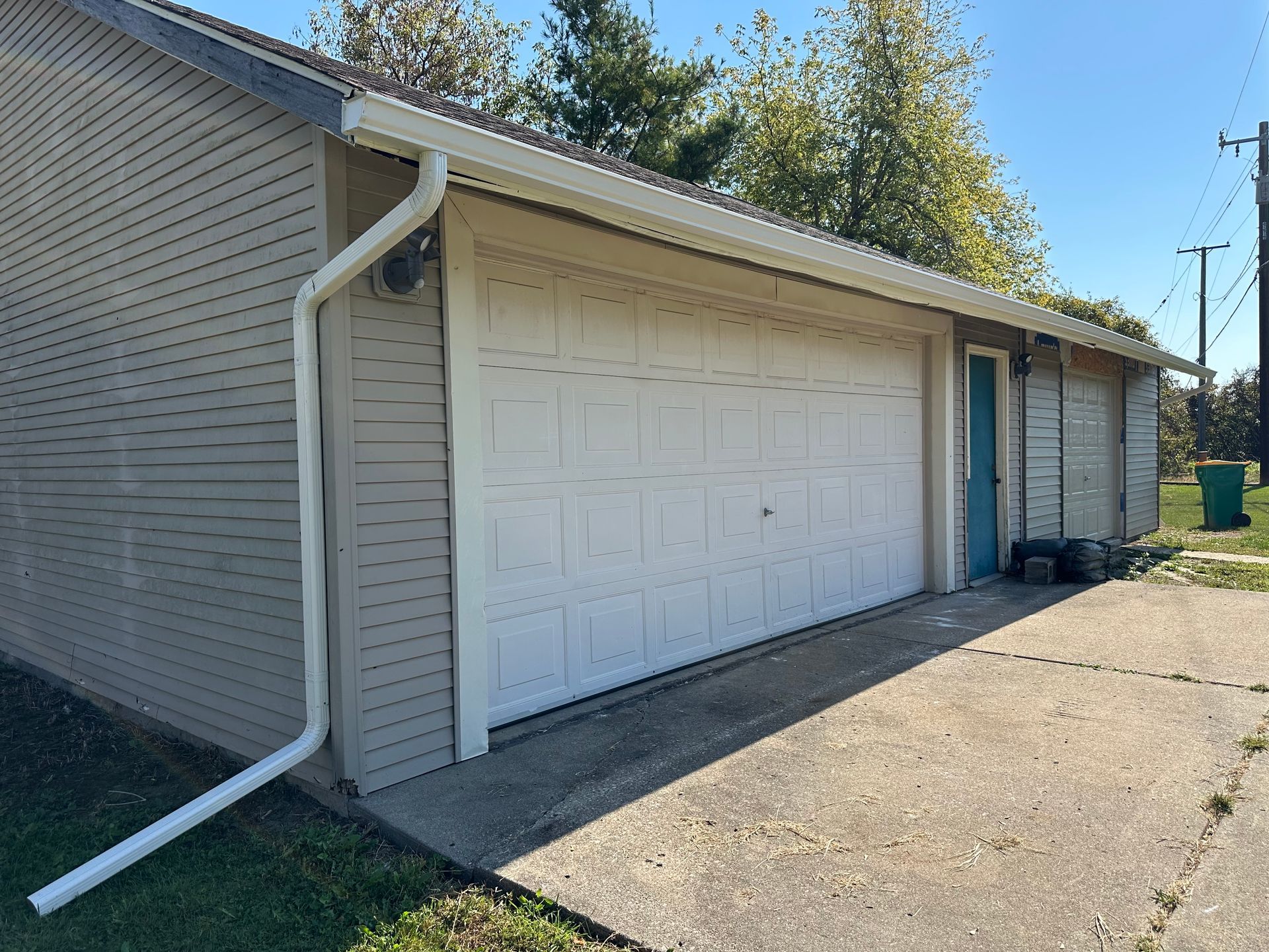 Garage with white door, tan siding, concrete driveway, and blue door.