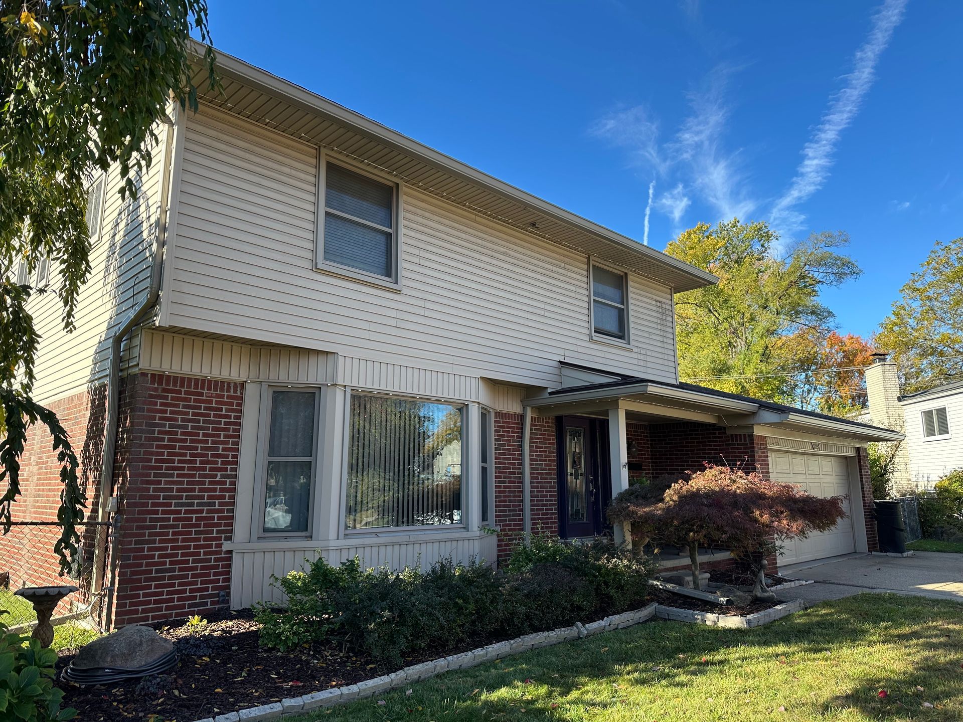 Two-story house with brick and siding, a covered entry, and a blue sky.