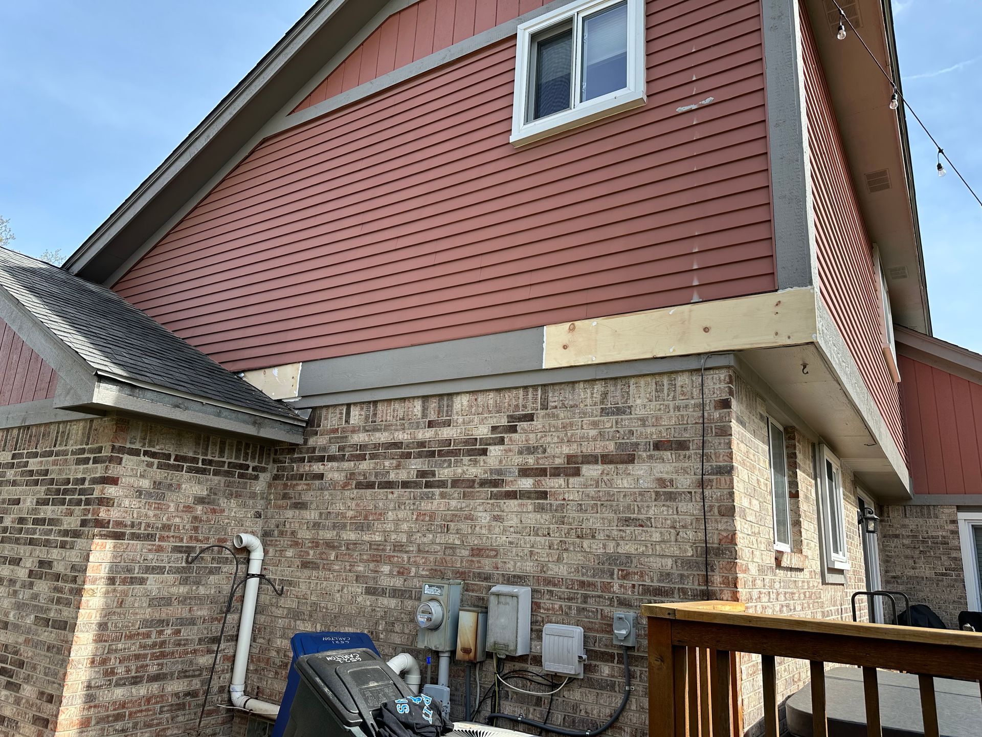Red siding on a brick building with a wooden deck; electrical boxes are visible below.