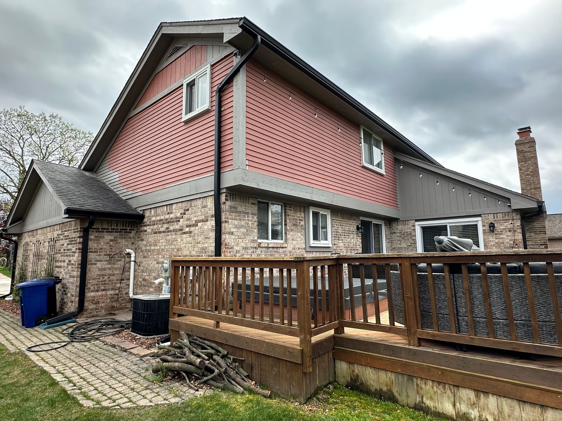 Brick and siding house with wooden deck; overcast sky.