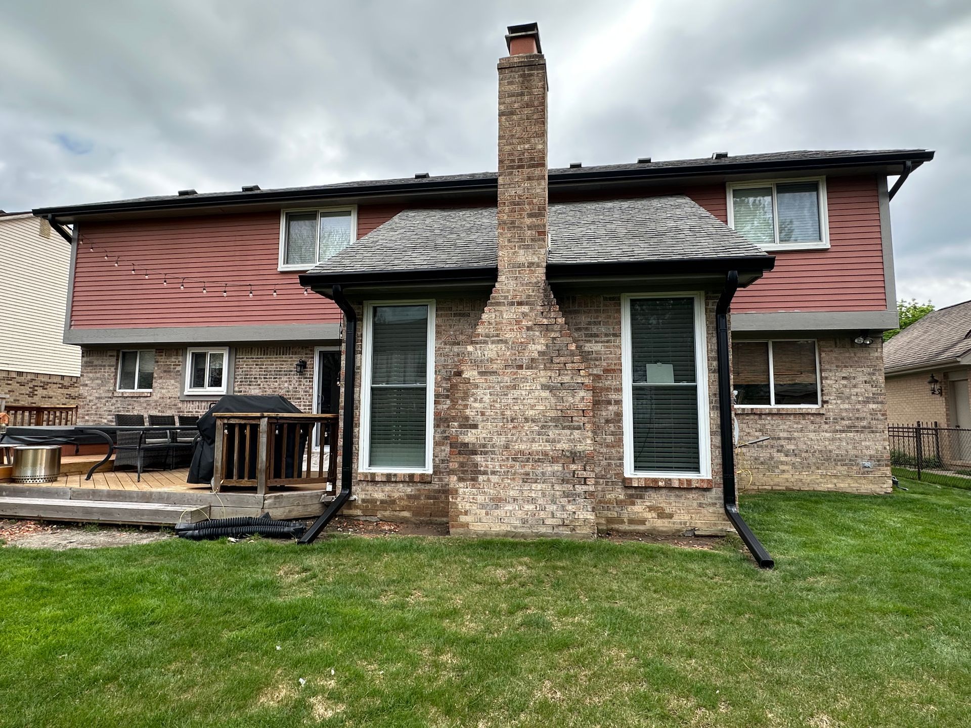 Back of a two-story brick house with a chimney and windows, a red wooden facade, and a green lawn.