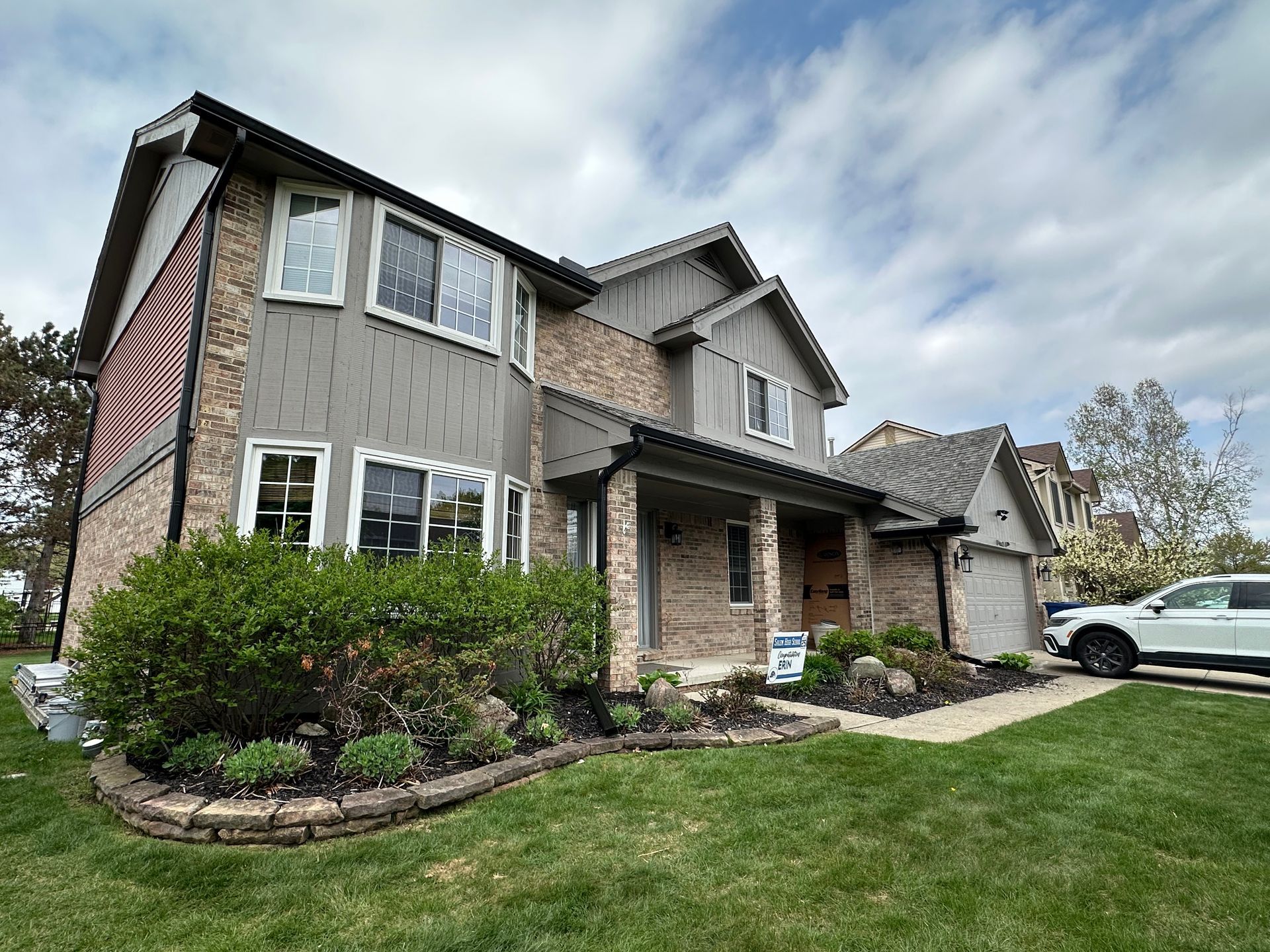 Two-story house with brick and gray siding, manicured lawn, and SUV parked in driveway.