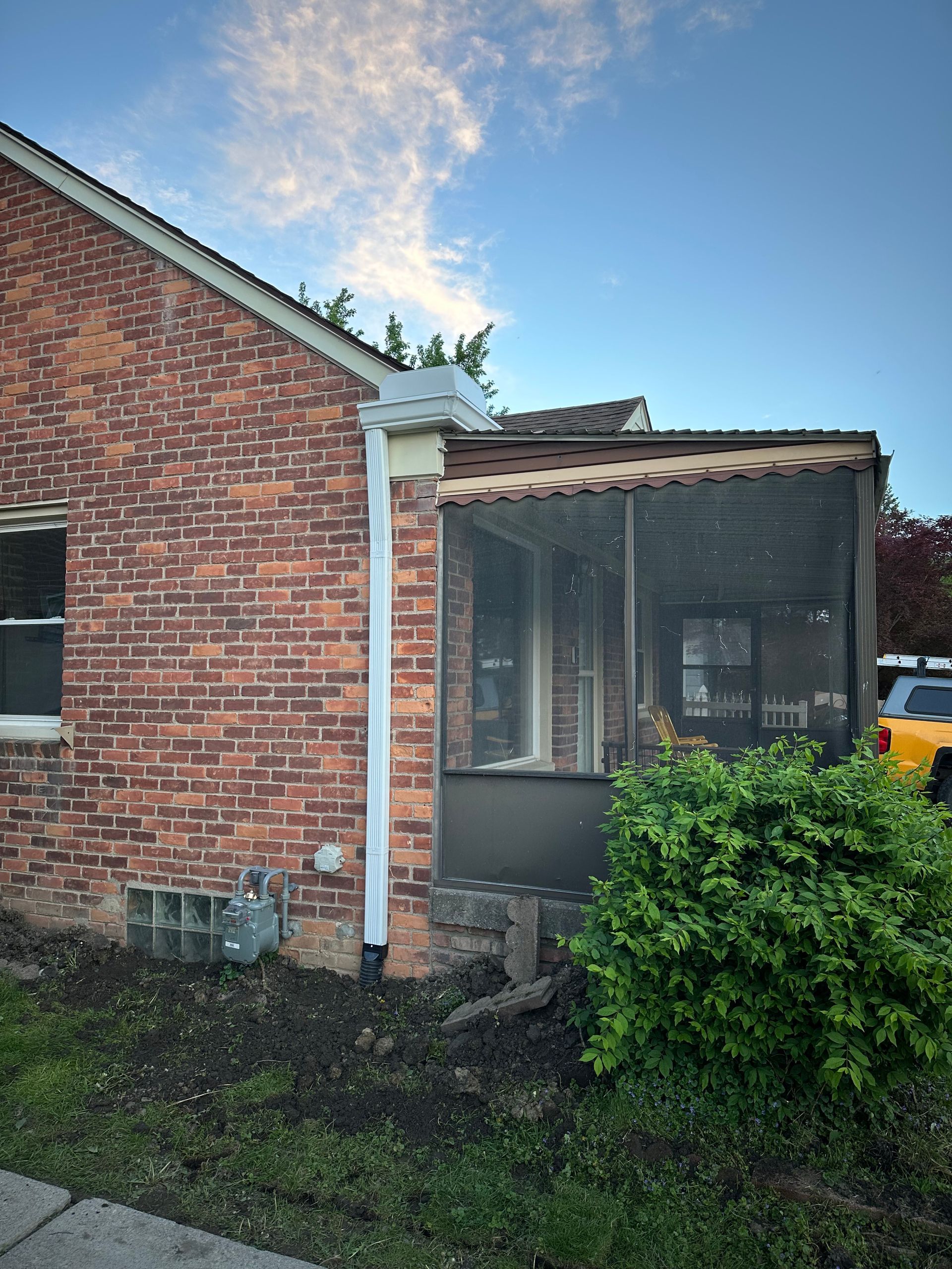 Brick house with a screened porch and a gutter. Overcast sky.