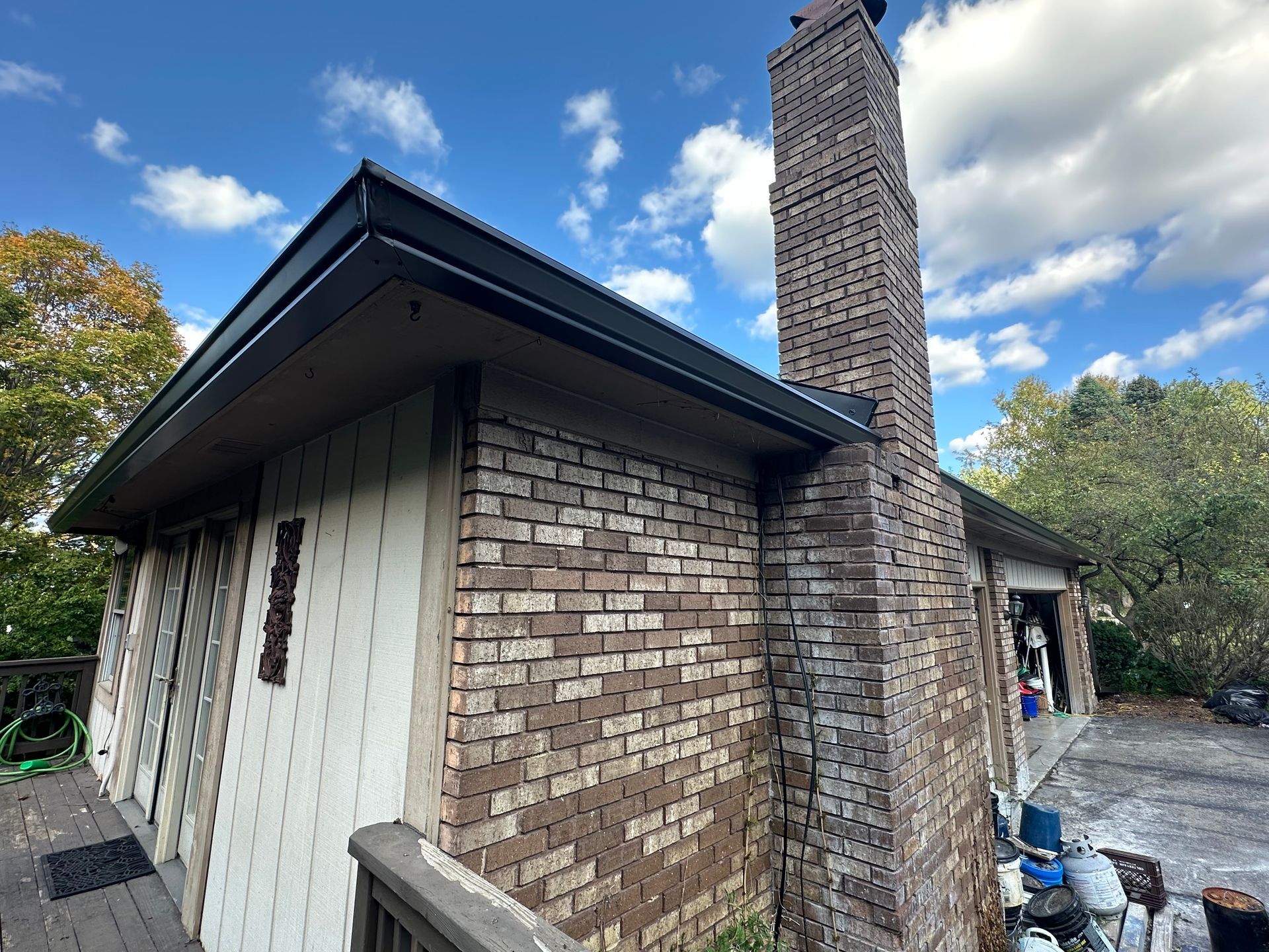 Brick house with a chimney and dark roof under a blue sky.