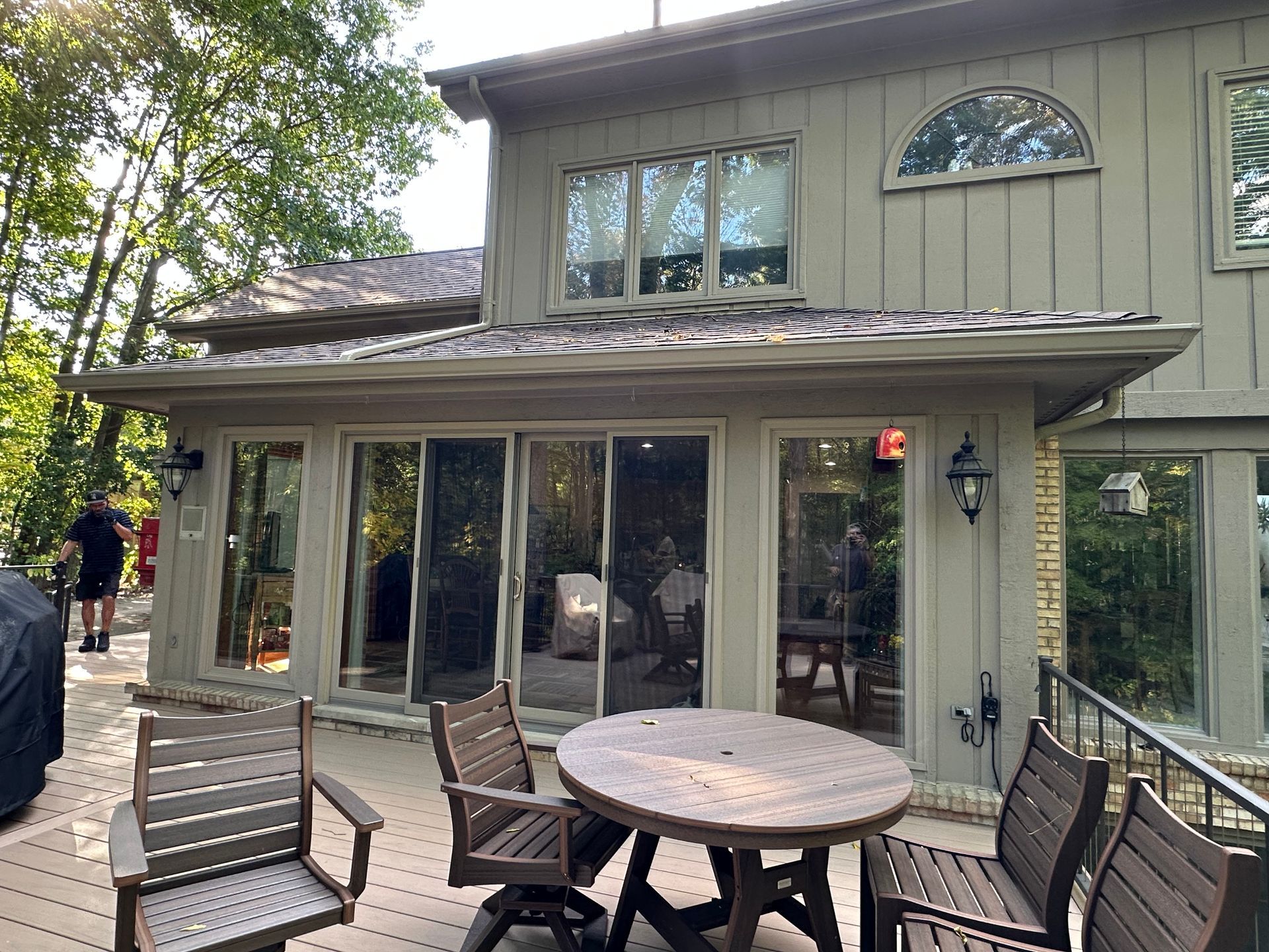 Back patio with wooden furniture, sliding glass doors, and a two-story house.