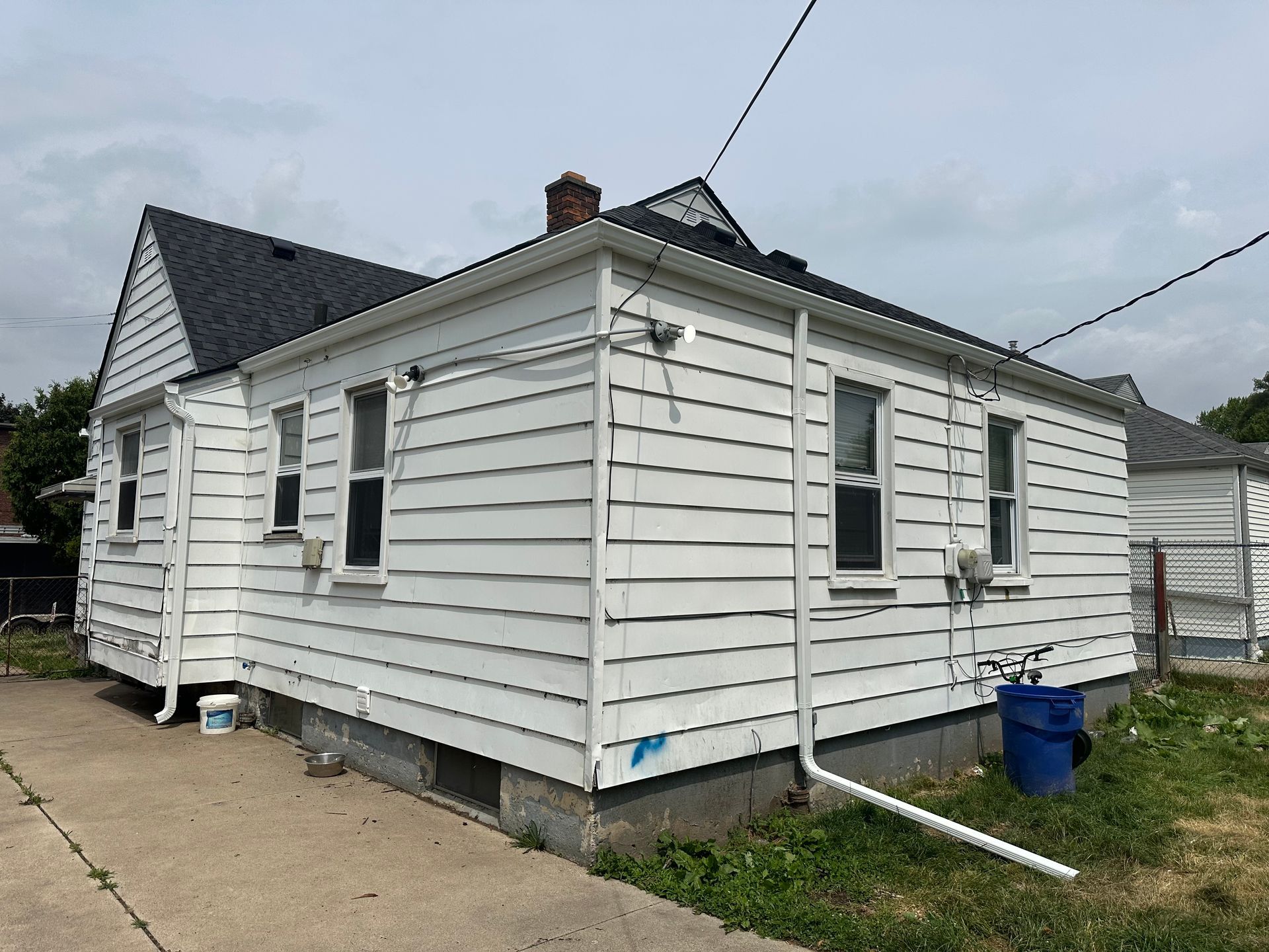 Side view of a white-sided house with a dark roof and several windows; overcast sky.