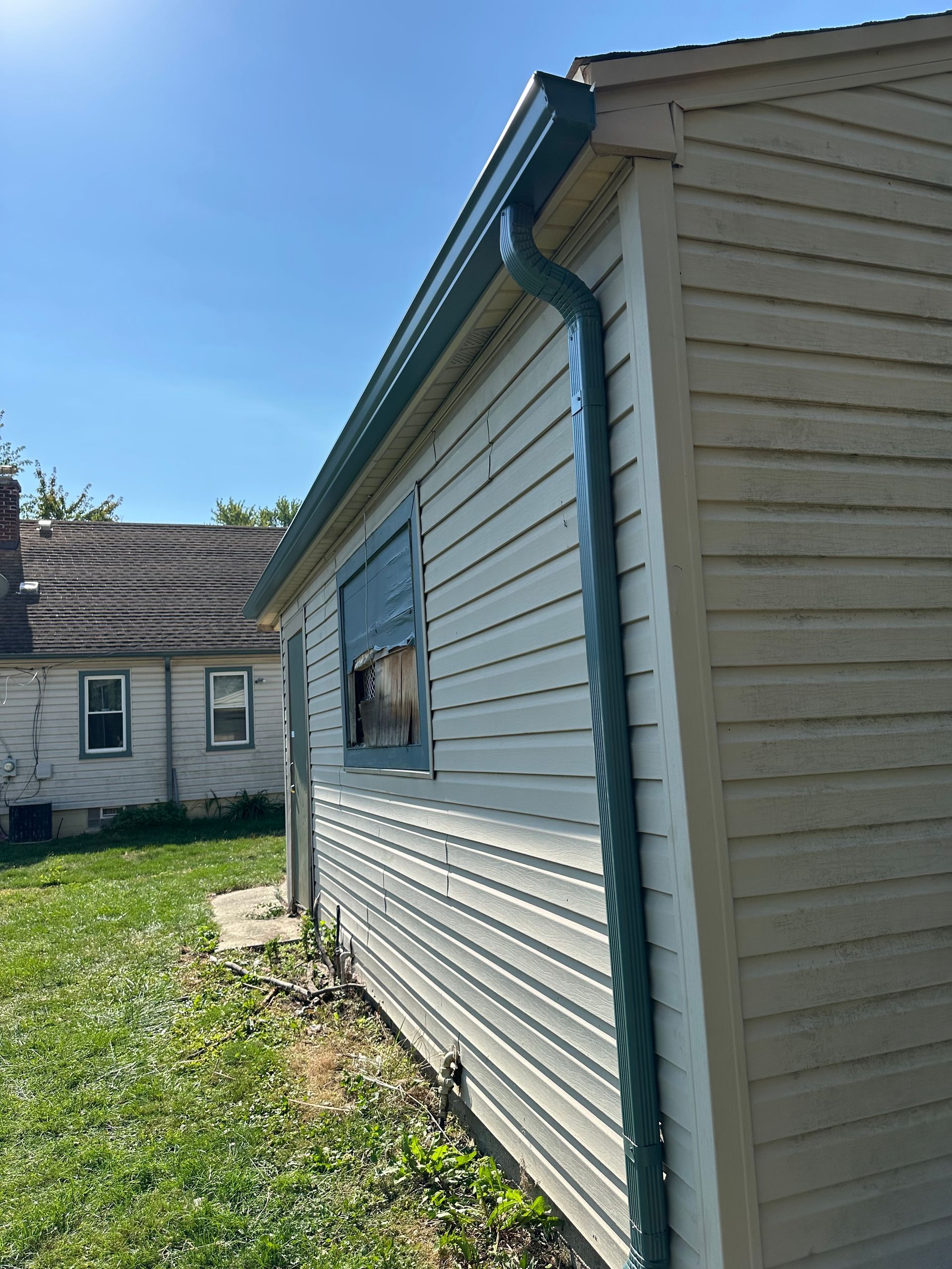 Side view of a weathered building with blue trim, gutter, and a damaged window, outdoors.