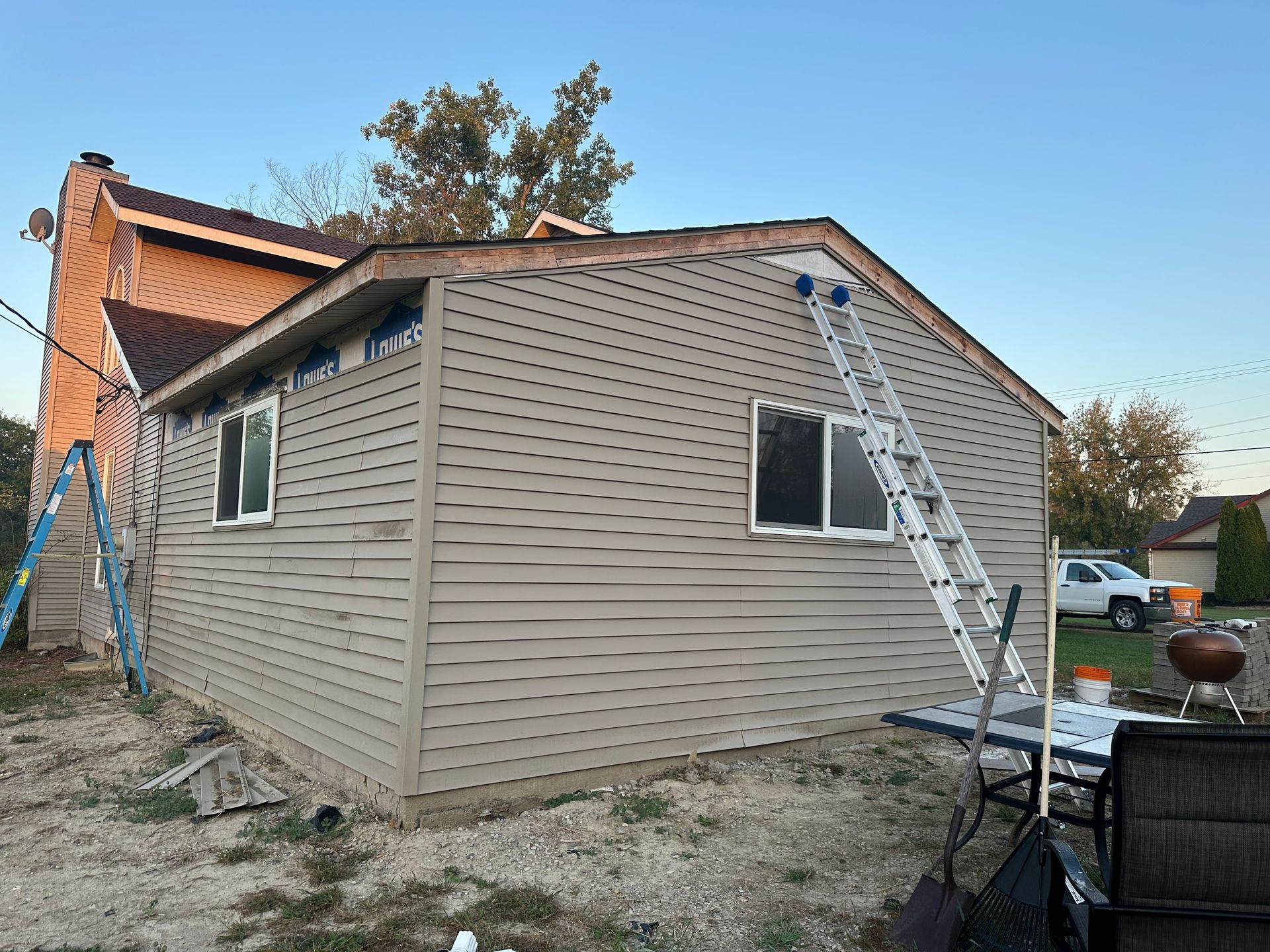 House with light brown siding under construction, ladders and tools present.