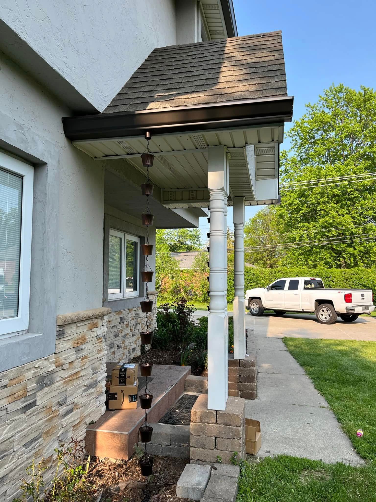 Exterior view of a house with a porch. Rain chains hang from the roof. A white truck is parked on the street.