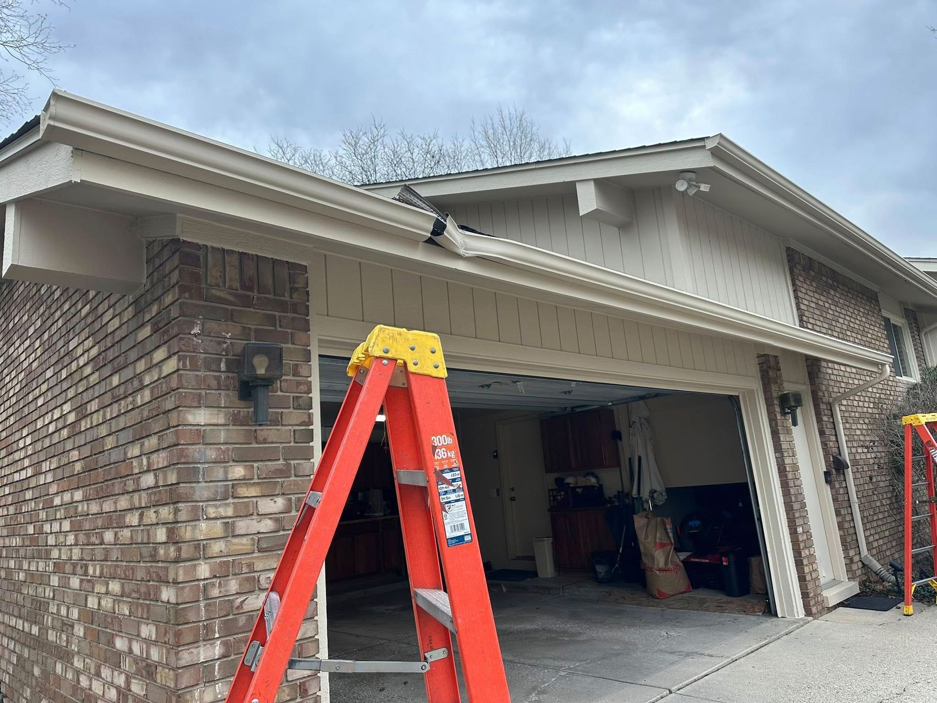 Garage exterior with a red ladder and light tan siding and brown brick.