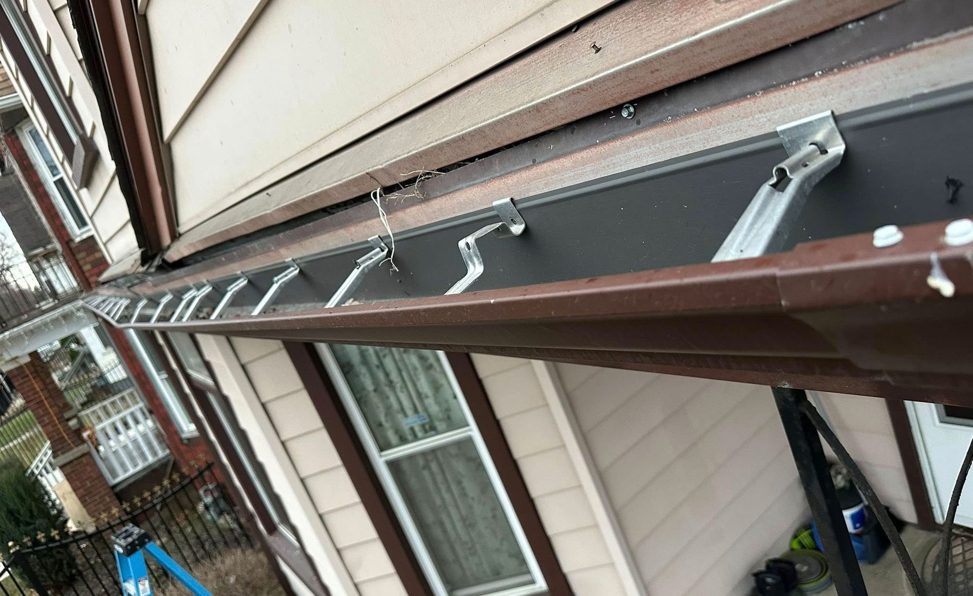 Brown gutters along the roof of a house with metal support brackets.
