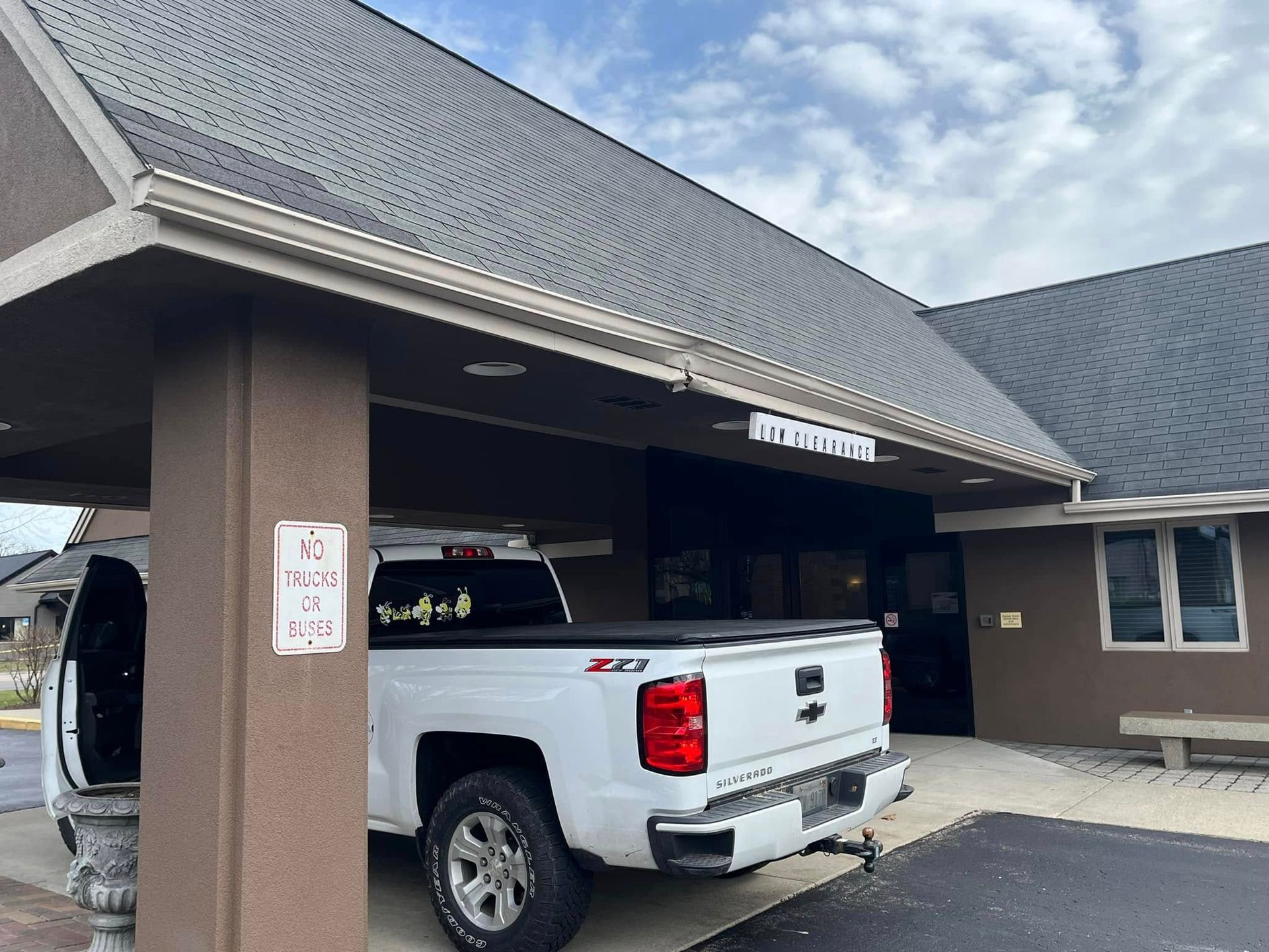 White pickup truck parked under a brown covered entrance to a building with dark roof. 