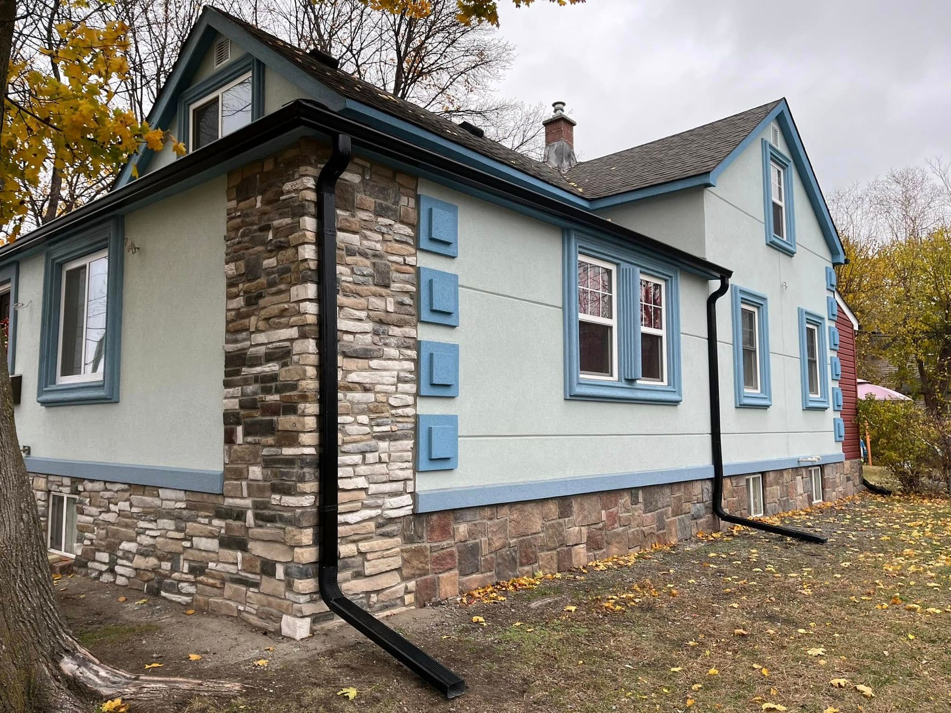 Two-story house with light blue siding, stone foundation, and black gutters under a cloudy sky.