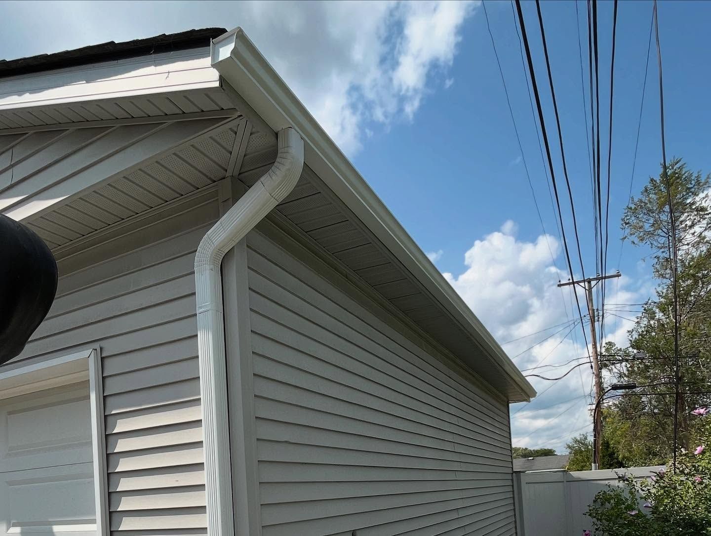 White siding with gutters, downspout, and overhead power lines under a partly cloudy sky.