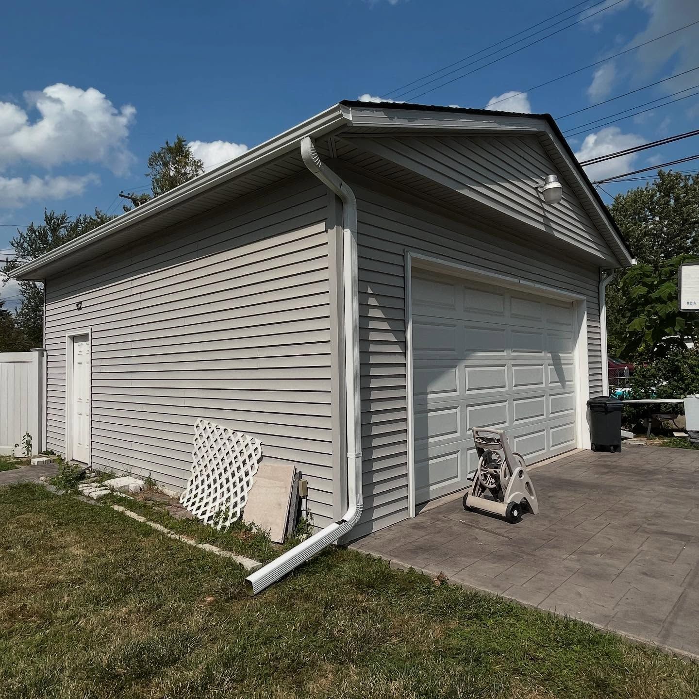 Gray detached garage with white trim, door, and overhead door, on a sunny day.