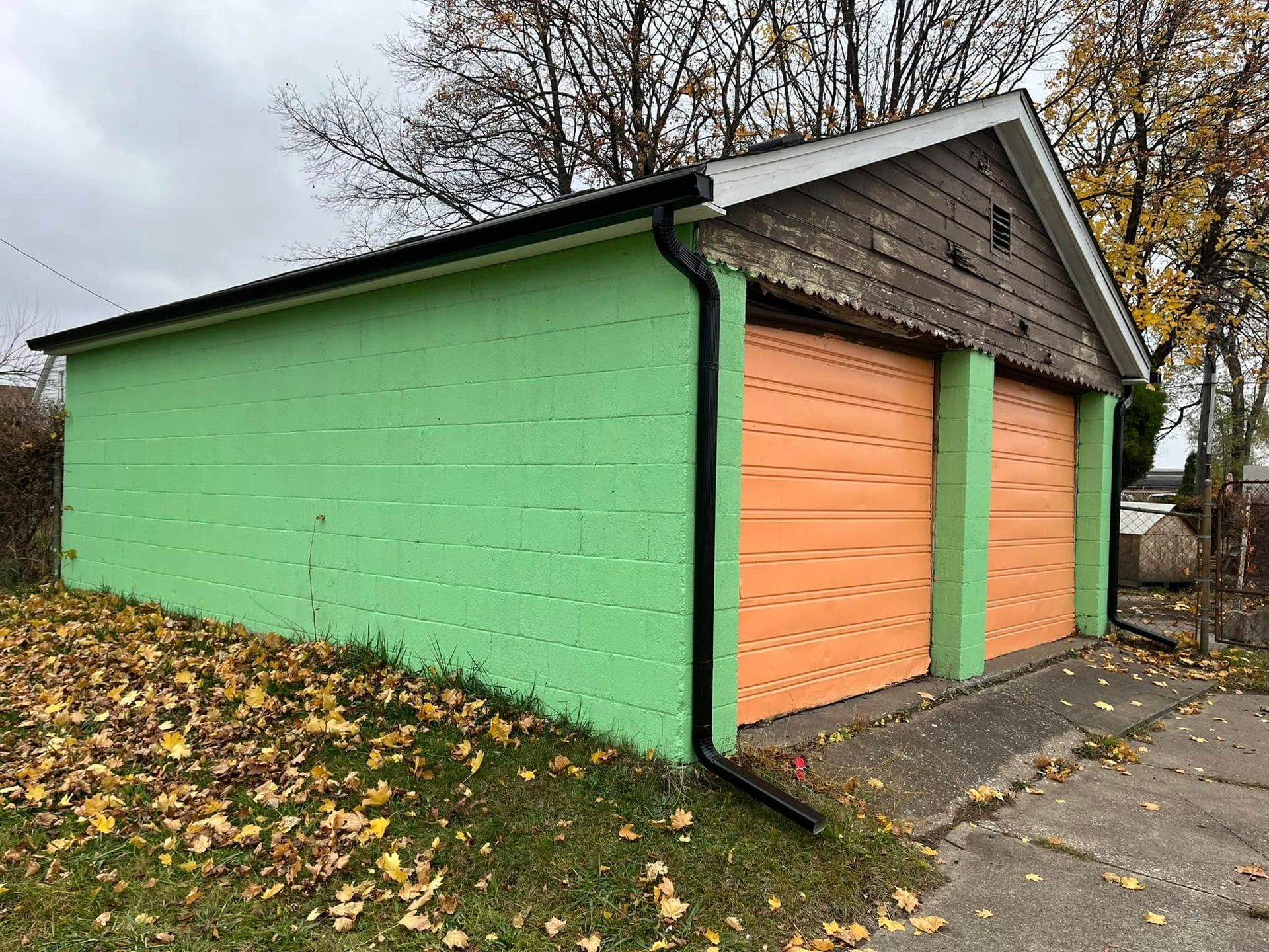 Green and orange garage with two doors, set on a concrete driveway.