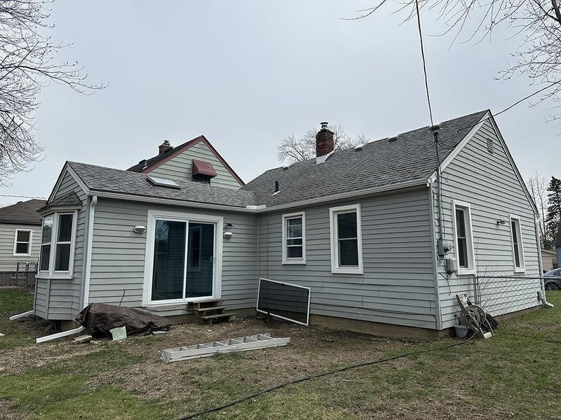 Gray house exterior with siding, a sliding glass door, and yard. Cloudy sky overhead.
