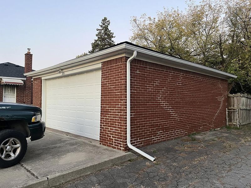 Brick garage with a white overhead door and white gutter, parked vehicle to the left.