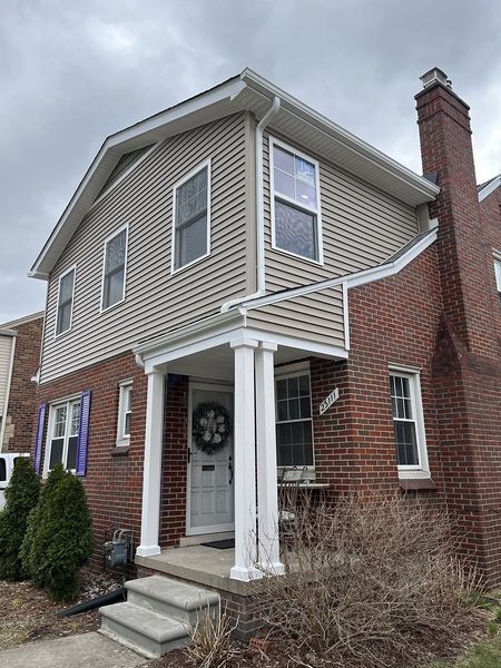 Two-story house with brick base, tan siding, white trim, and a porch.