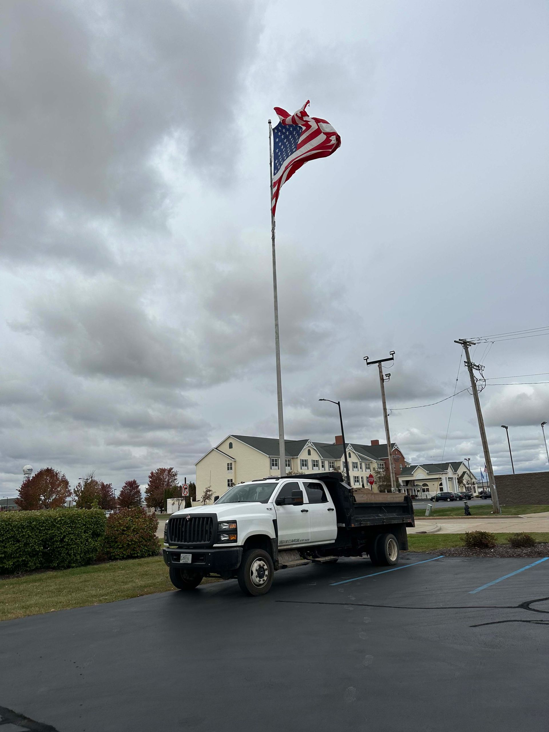 A dump truck is parked next to an american flag on a pole