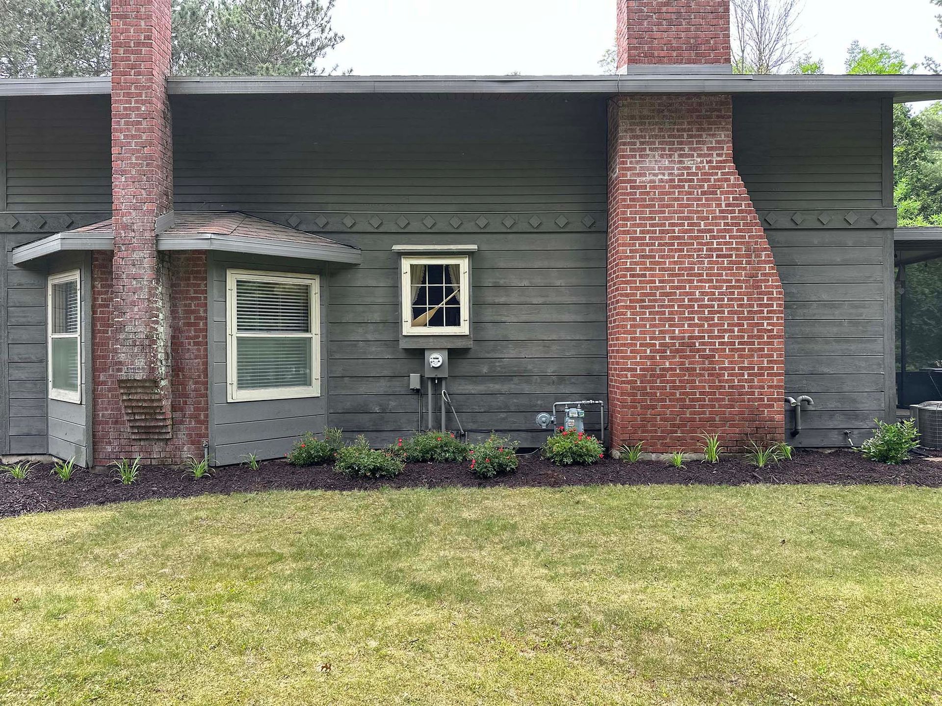 A house with a brick chimney and a gray siding is sitting on top of a lush green lawn.
