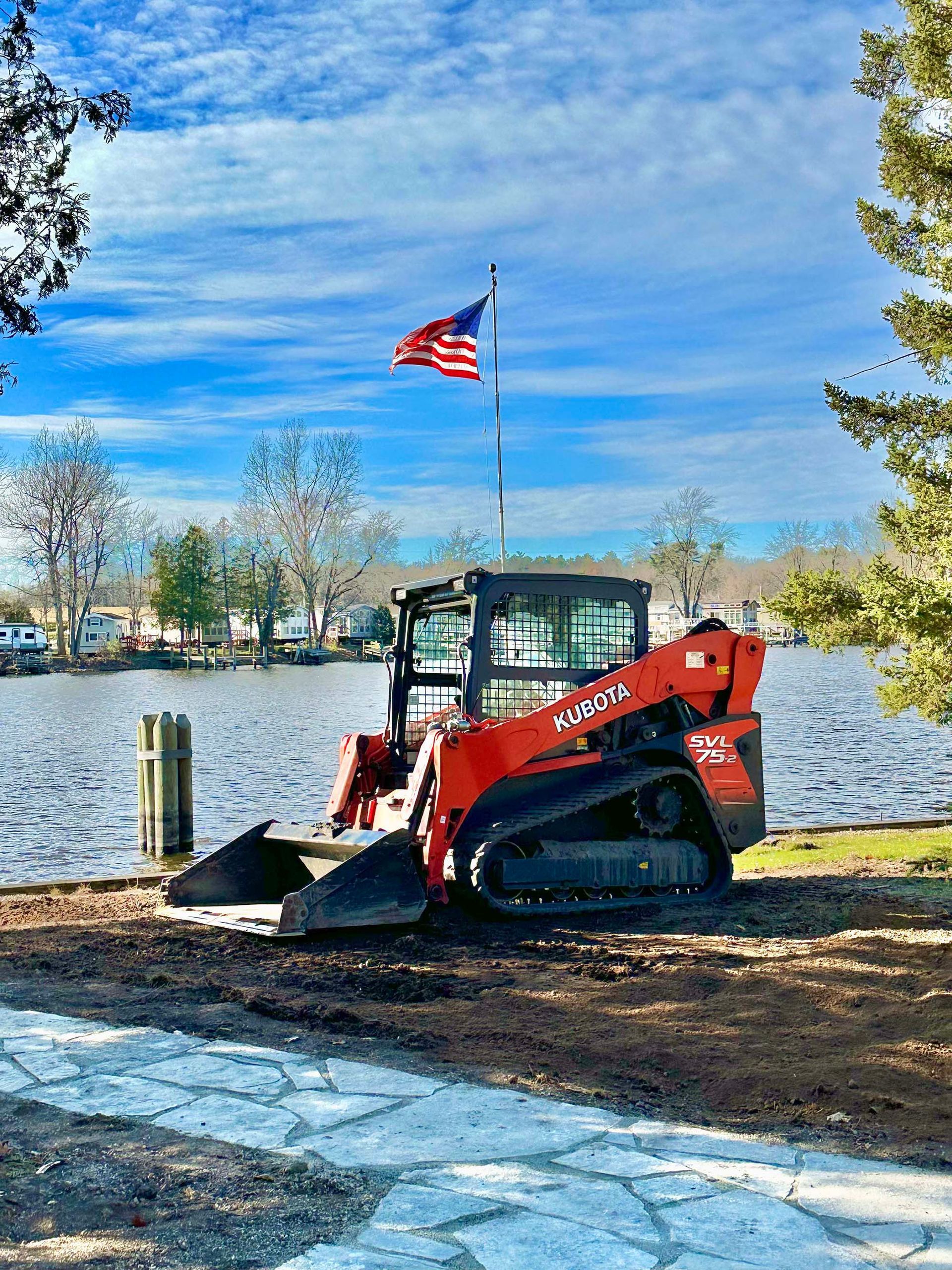 A bulldozer is parked next to a lake with an american flag on top of it.