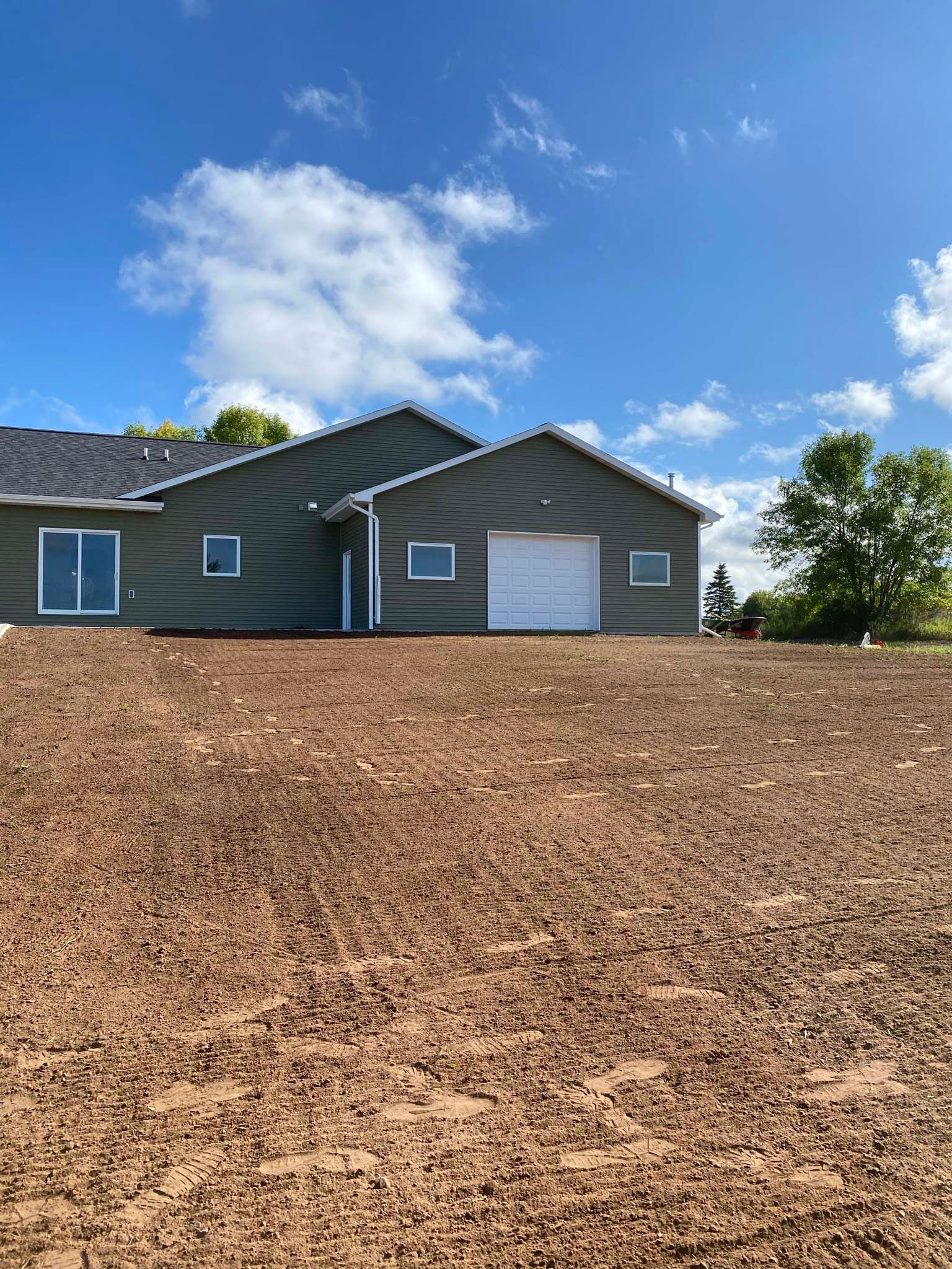 A house with a garage door is sitting on top of a dirt field.