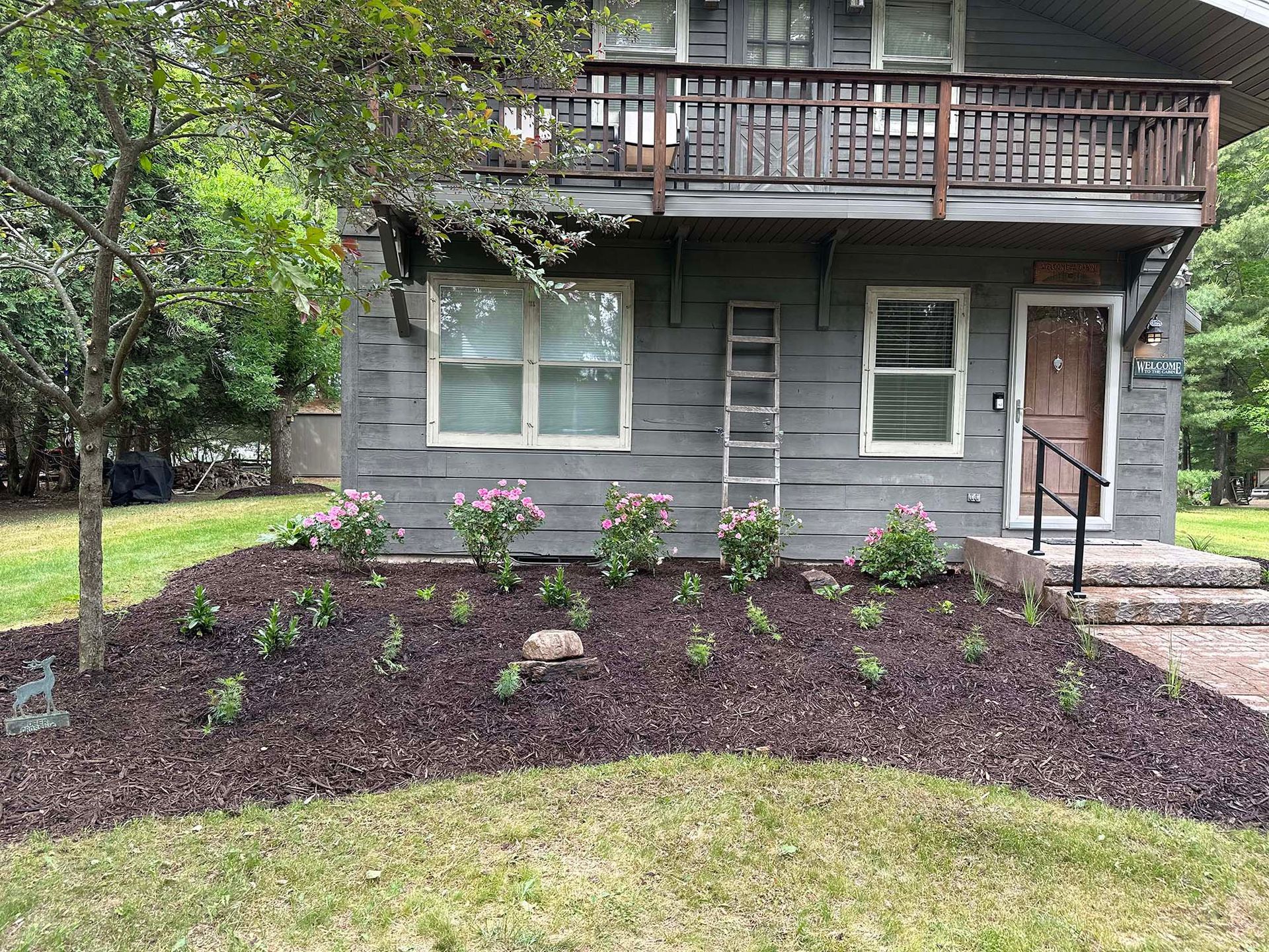 A gray house with a deck and flowers in front of it.