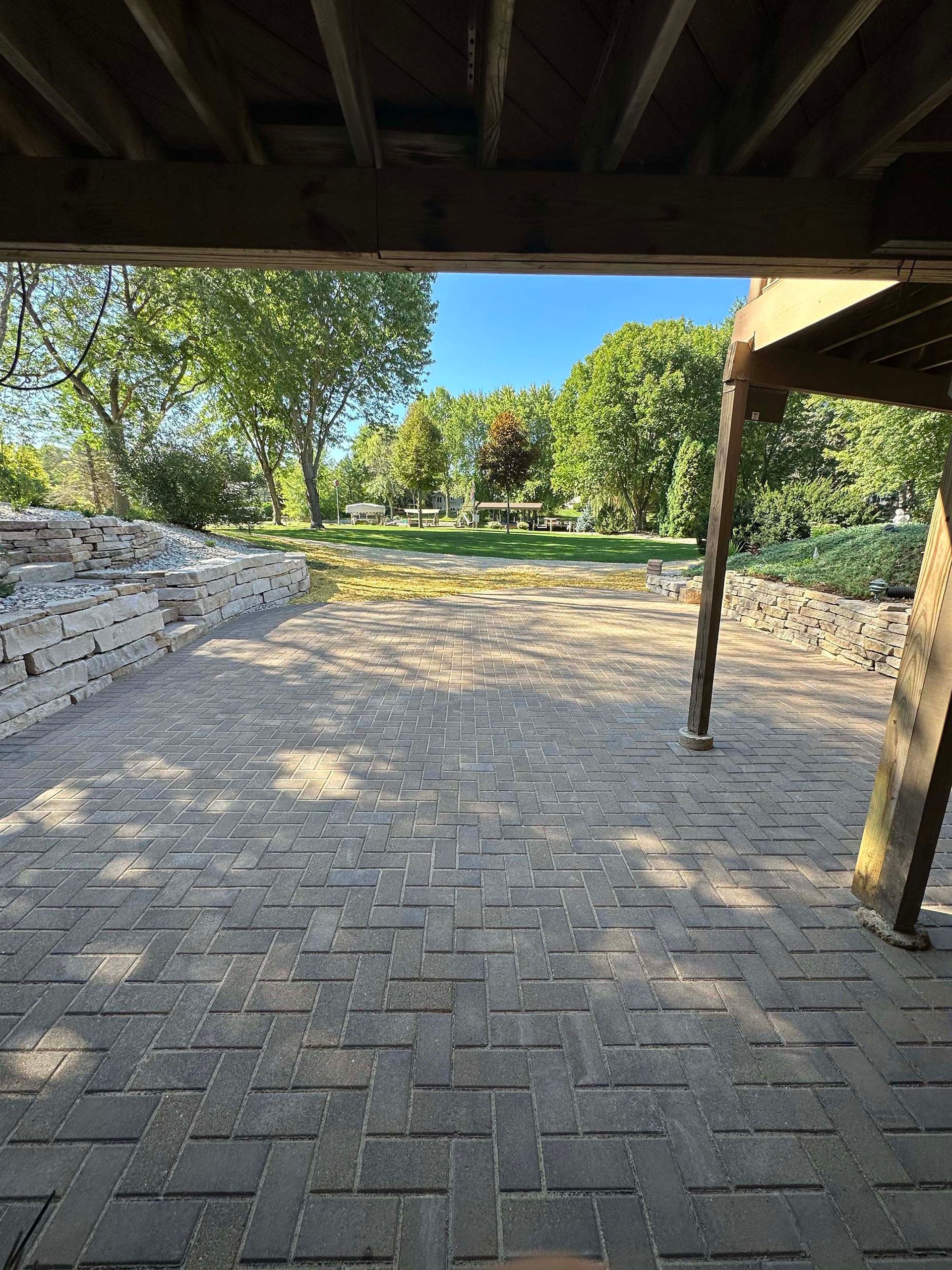 A brick patio under a wooden deck with trees in the background.