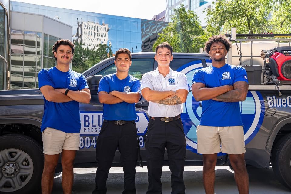 Four people in blue shirts with arms crossed stand in front of a blue and black truck with a logo.